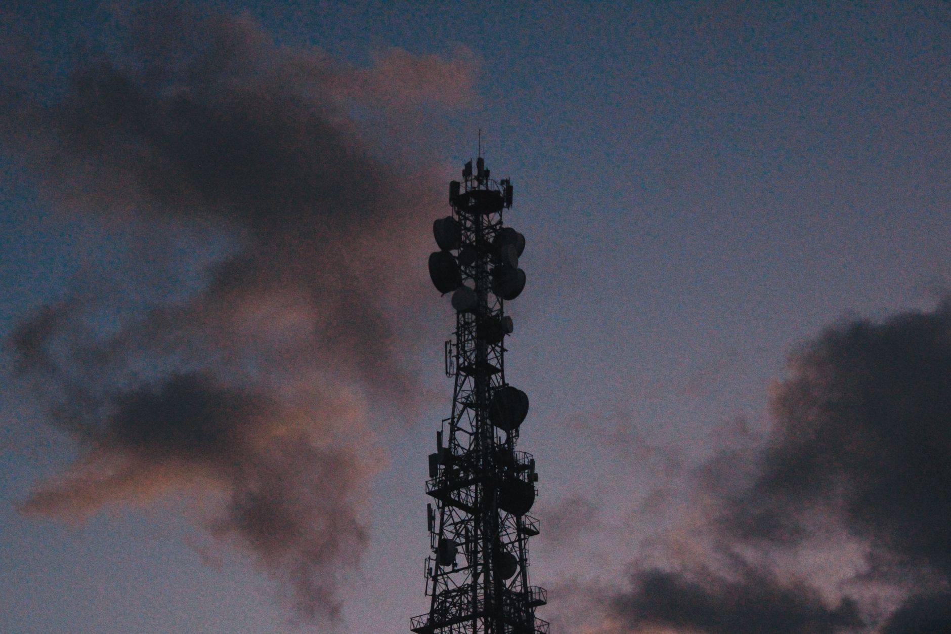 aerial view of a wireless network tower rising above a suburban commercial district with fiber conduit visible at the base