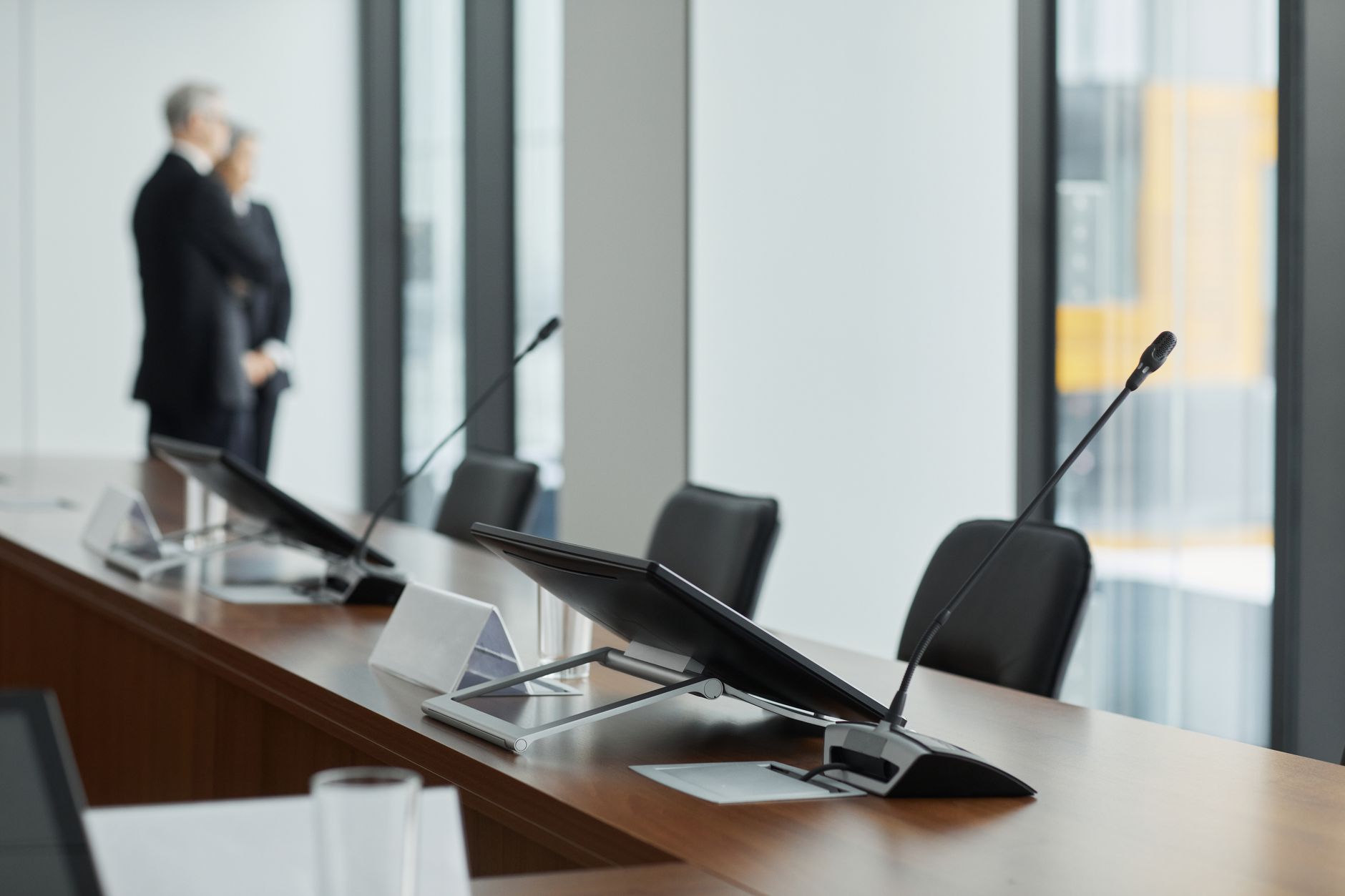 wide shot of a corporate annual general meeting venue, empty chairs arranged in rows facing a presentation screen displaying financial charts, natural light through tall windows