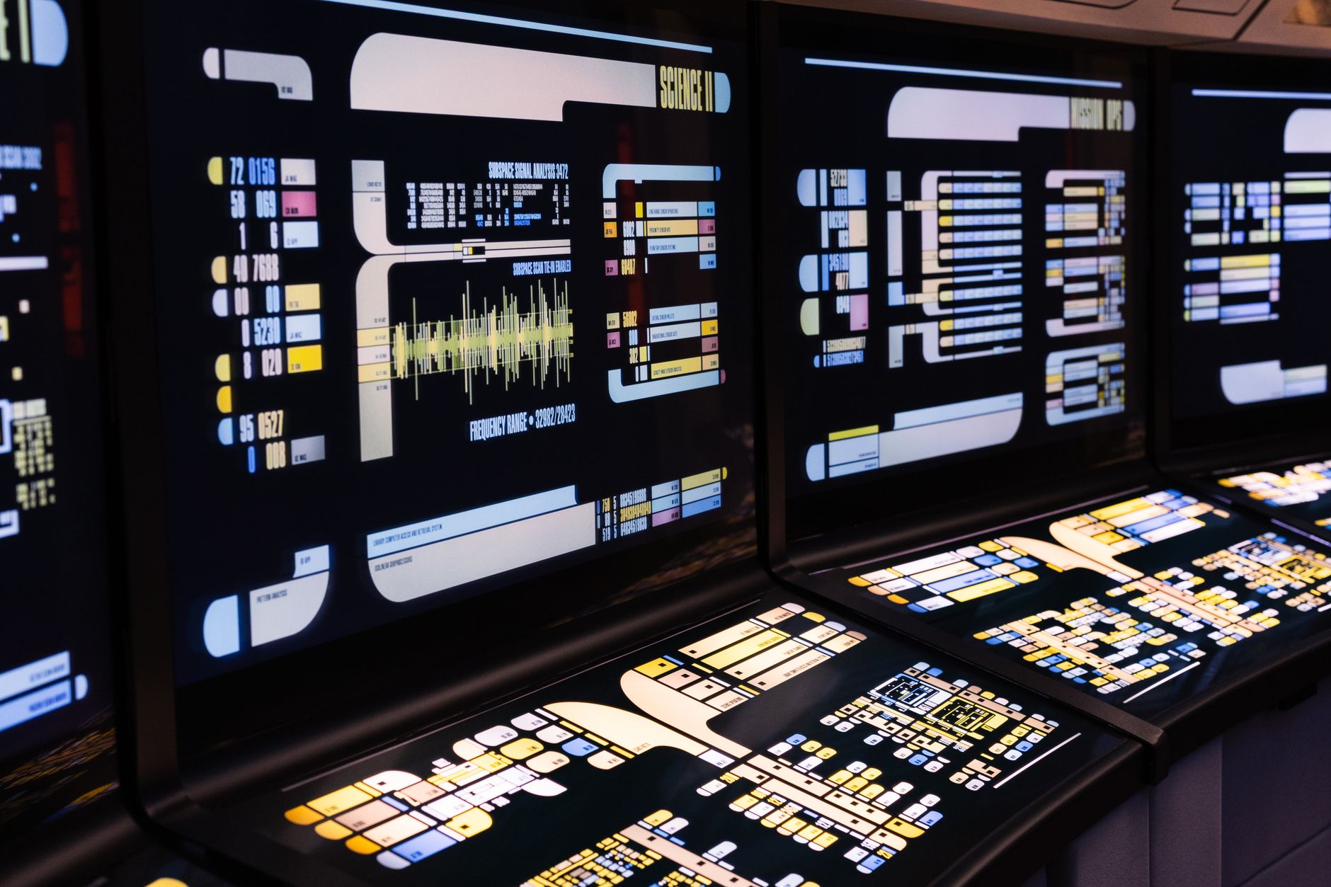 a network operations center with multiple monitors displaying system topology maps and alert dashboards, dimly lit with overhead fluorescent lighting
