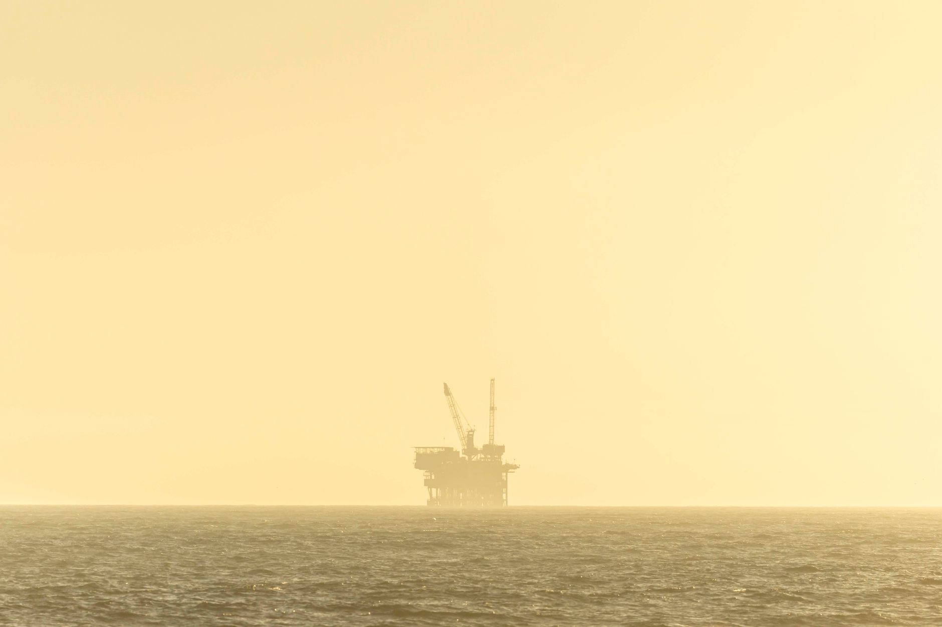 aerial view of a deepwater oil platform in the Gulf of Mexico at golden hour, surrounded by calm open water with supply vessels visible in the distance