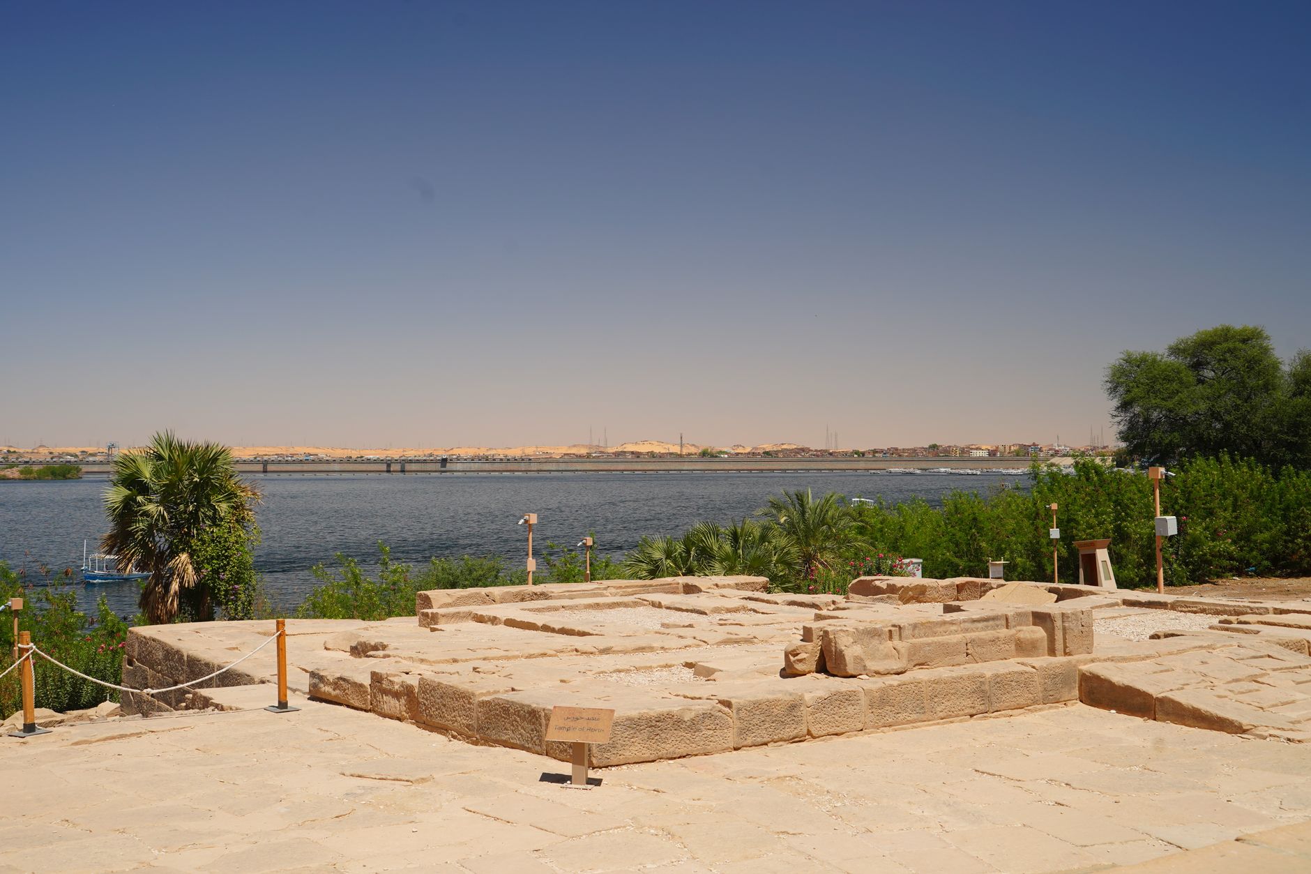a view across the Egyptian desert toward the Nile River valley at dusk, with a clear open sky stretching to the horizon and ancient stone structures visible in the distance