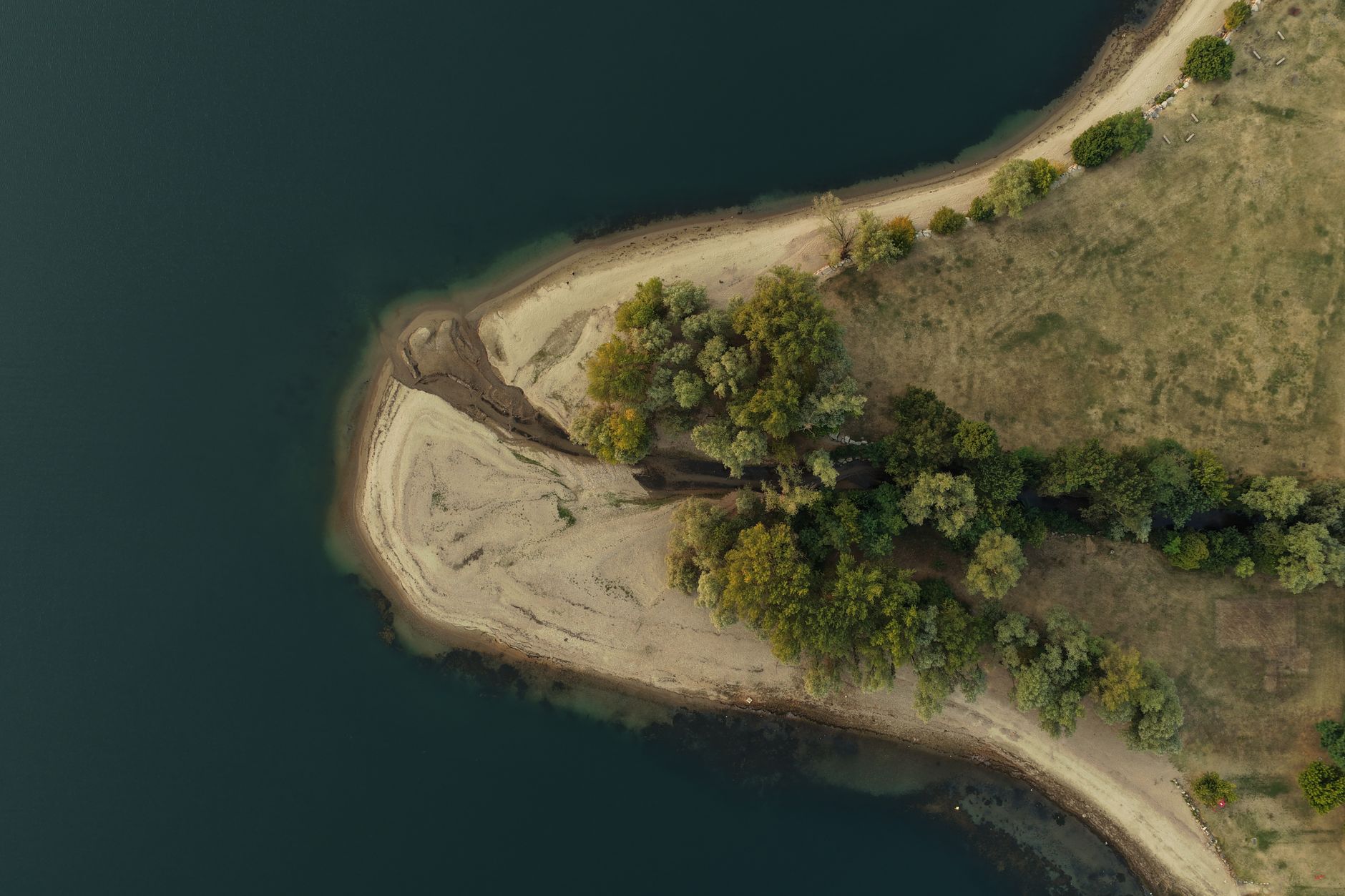 aerial view of a nuclear power plant situated along a wide river, with low water levels visibly exposing sandbars and dry riverbanks in the foreground