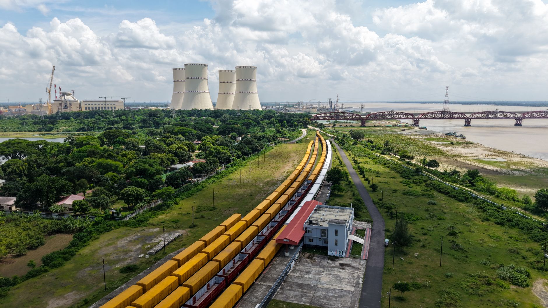 aerial view of a large nuclear power plant complex beside a river, with cooling towers emitting steam against a pale sky