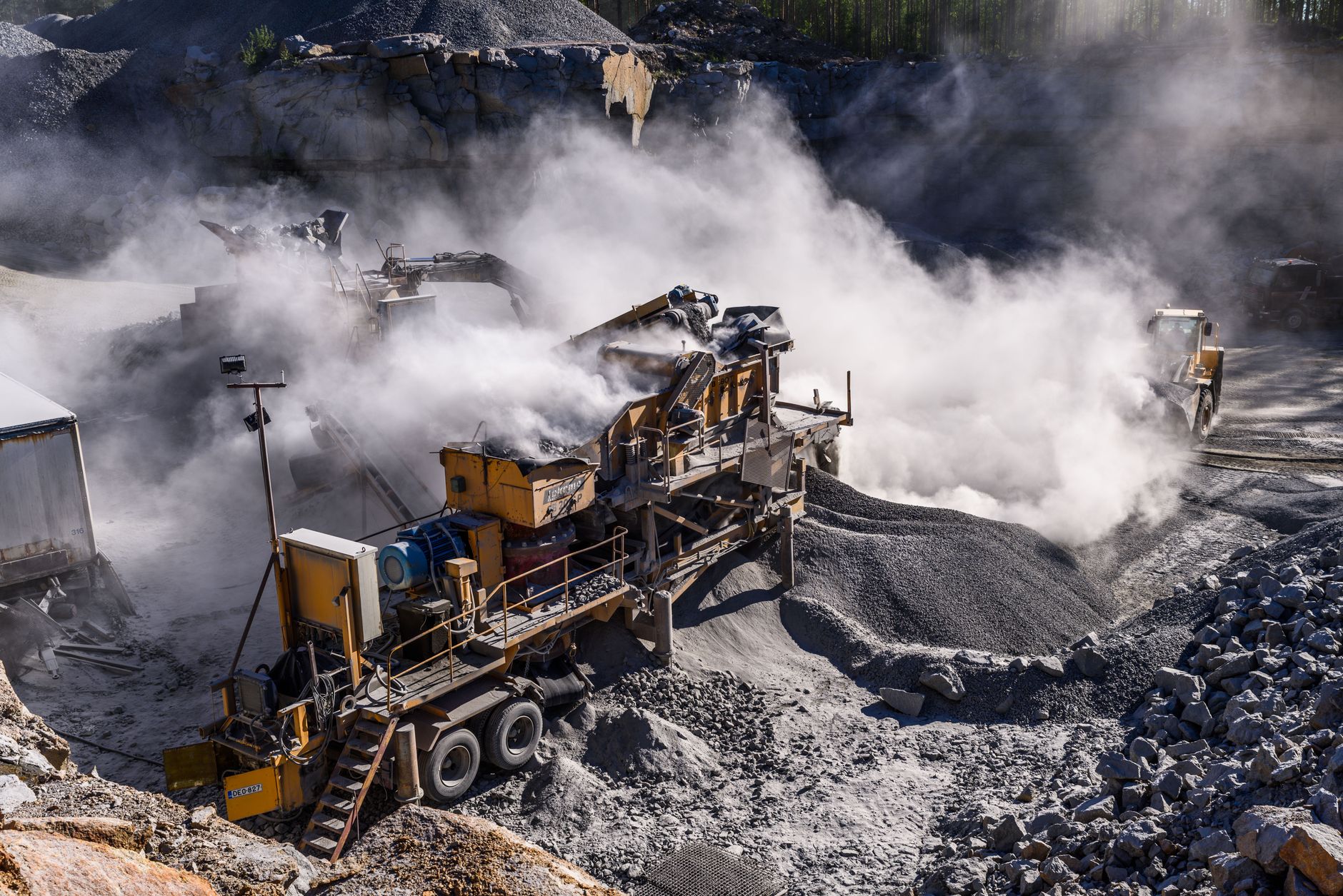 open-pit gold mine at dawn with excavation equipment operating on terraced rock faces, dust rising from haul roads