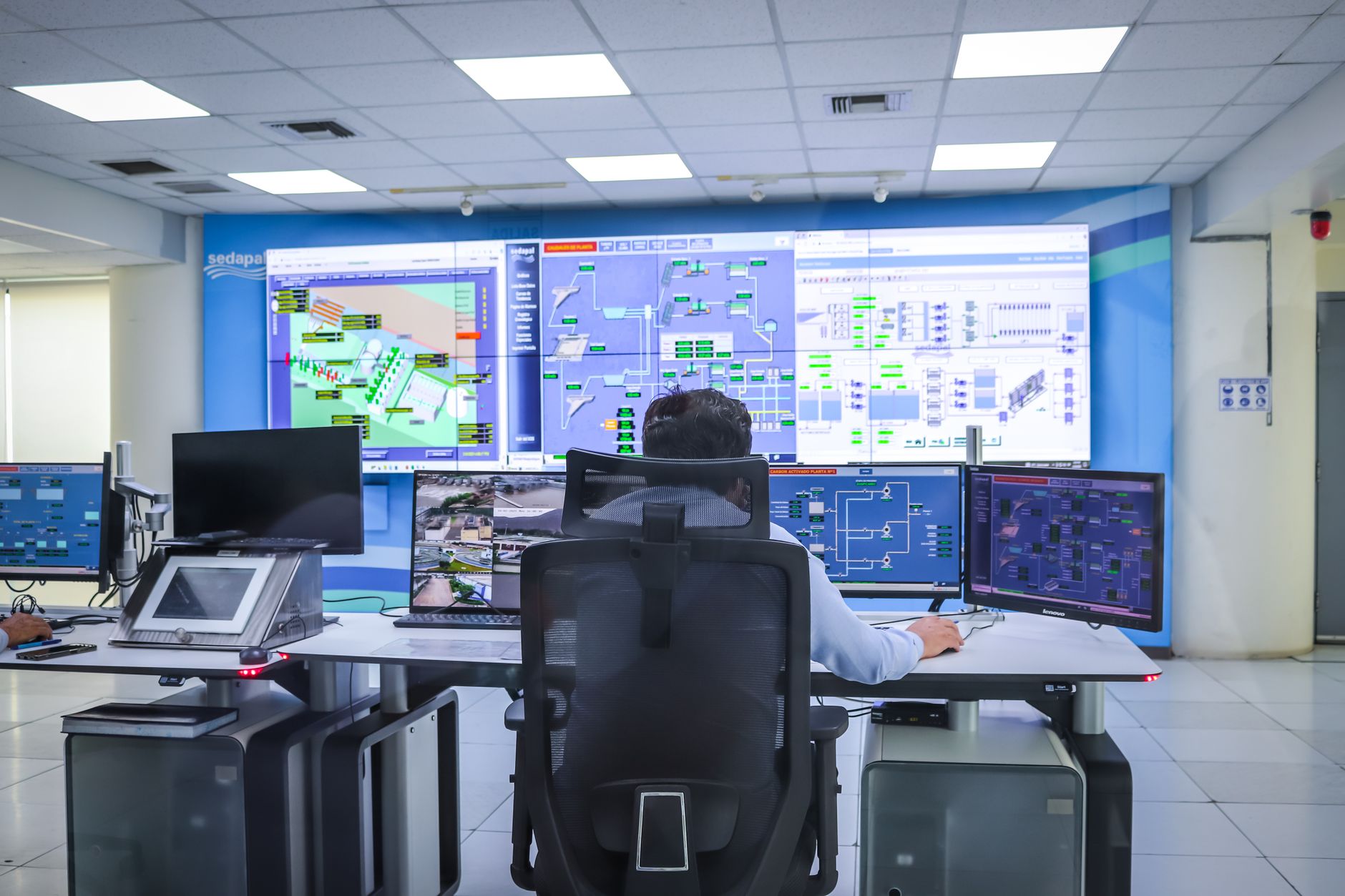 a wide-angle view of an open-plan security operations center at night, multiple curved monitors displaying network traffic graphs and alert dashboards, no people in frame