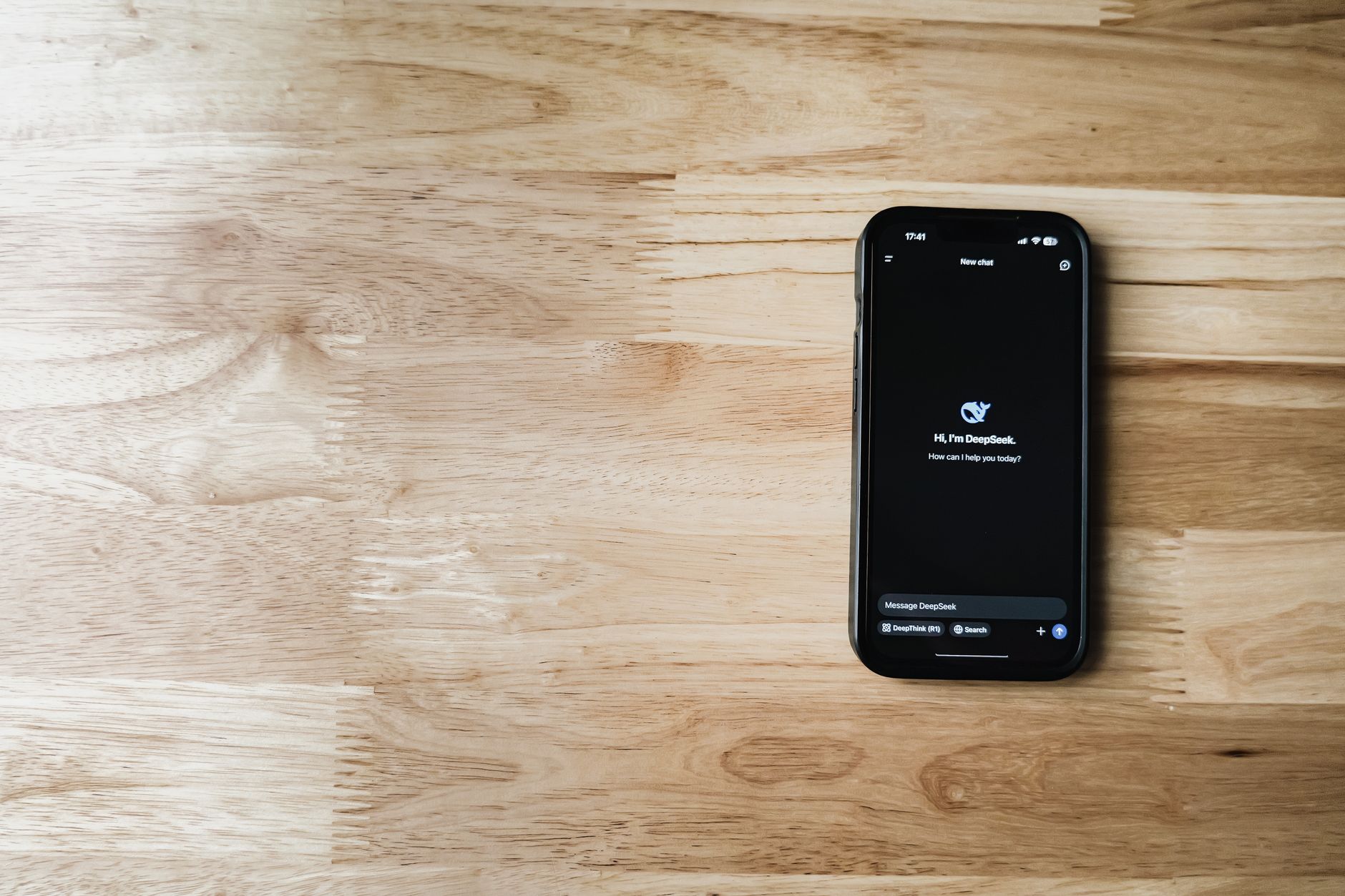 a close-up of a matte black smart ring resting on a wooden surface next to a smartphone displaying health metrics on screen