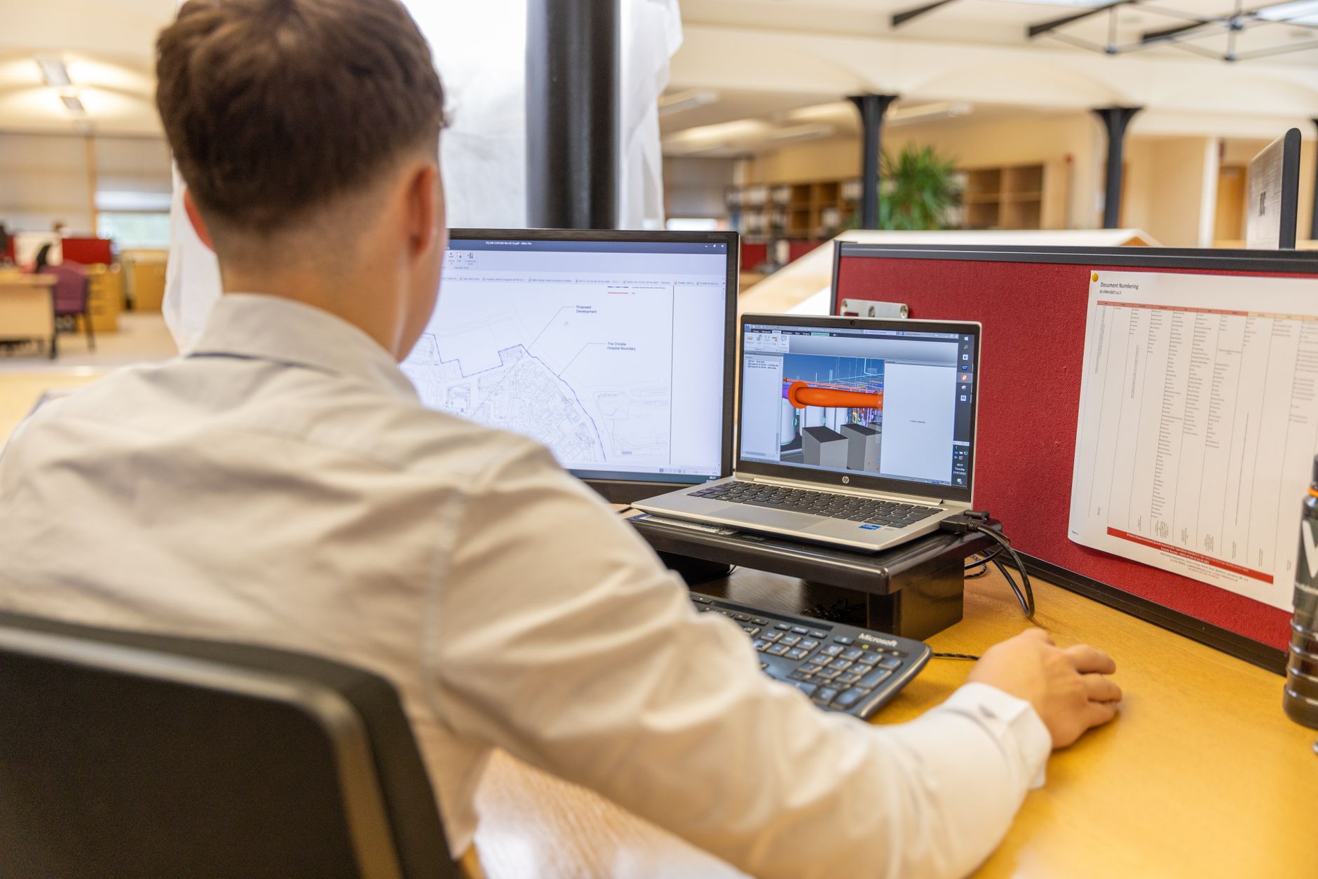 a wide-angle view of multiple monitor workstations displaying project timeline dashboards and resource allocation charts in a modern open-plan office