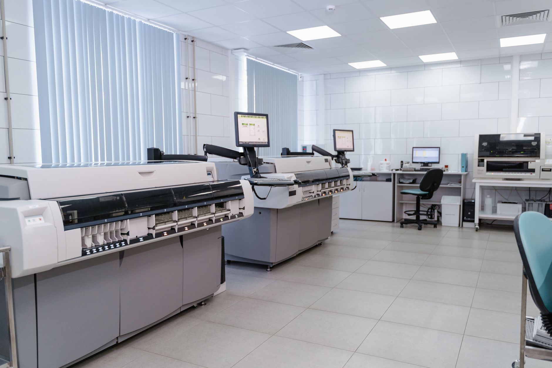 rows of workstations inside a pharmaceutical research facility with dual-screen setups showing genomic data and statistical modeling dashboards