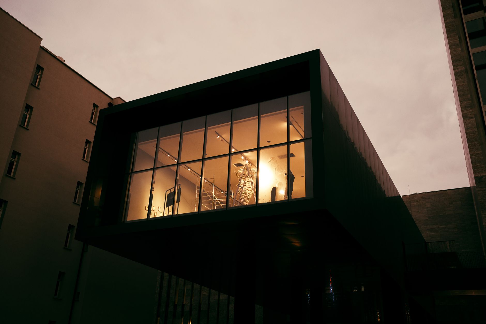 a modern pharmaceutical research facility exterior at dusk, with glass-walled office floors lit from within and a courtyard visible below