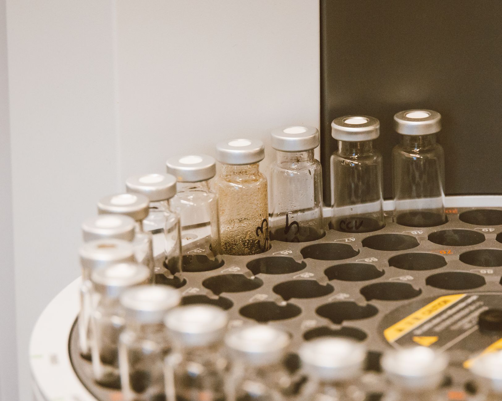 a sterile pharmaceutical laboratory with rows of compound synthesis equipment, glass vials, and robotic pipetting arms under white fluorescent lighting