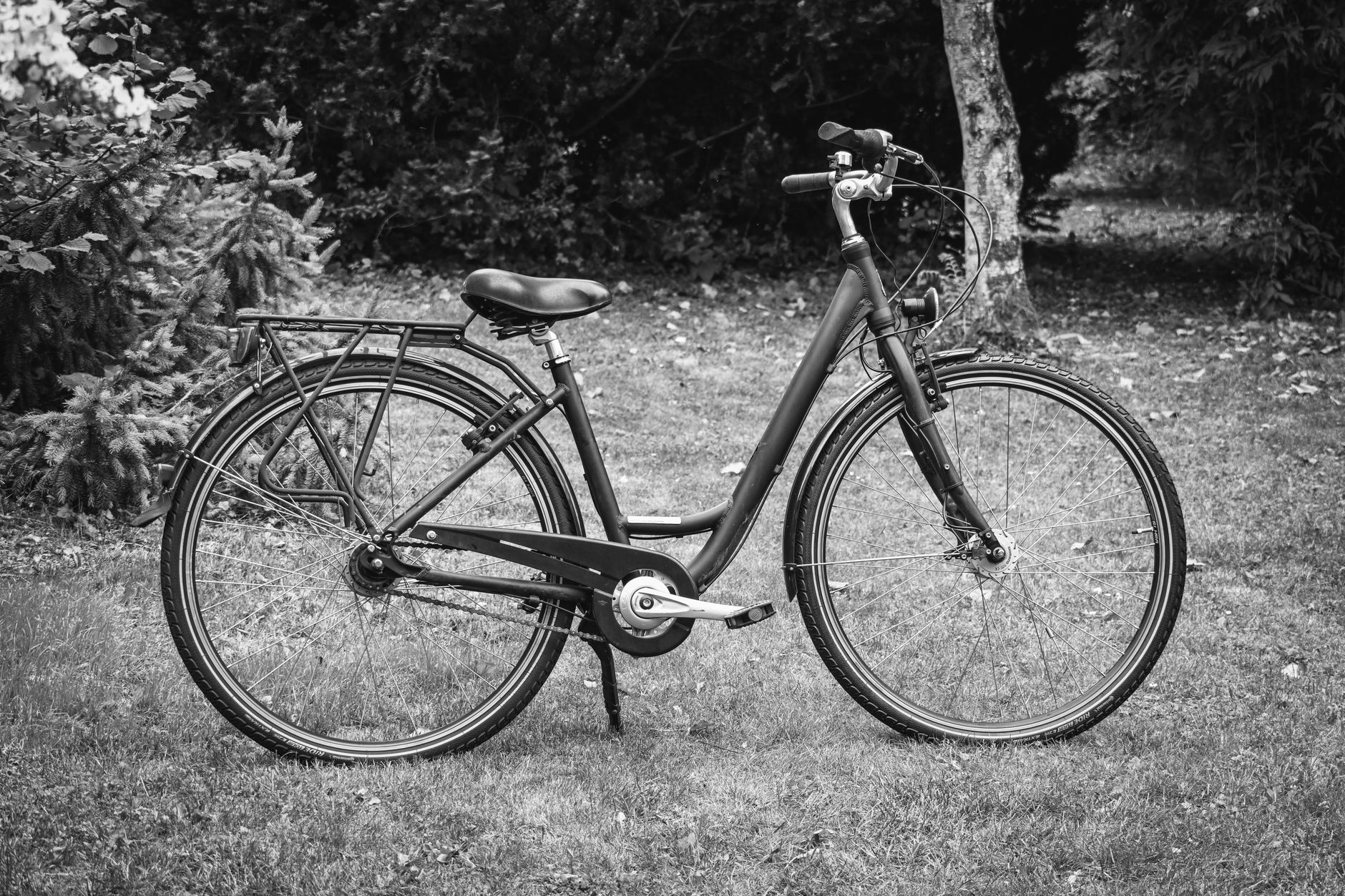 A matte-finish step-through e-bike parked against a brick urban wall, rear hub motor and integrated rear rack visible in natural daylight