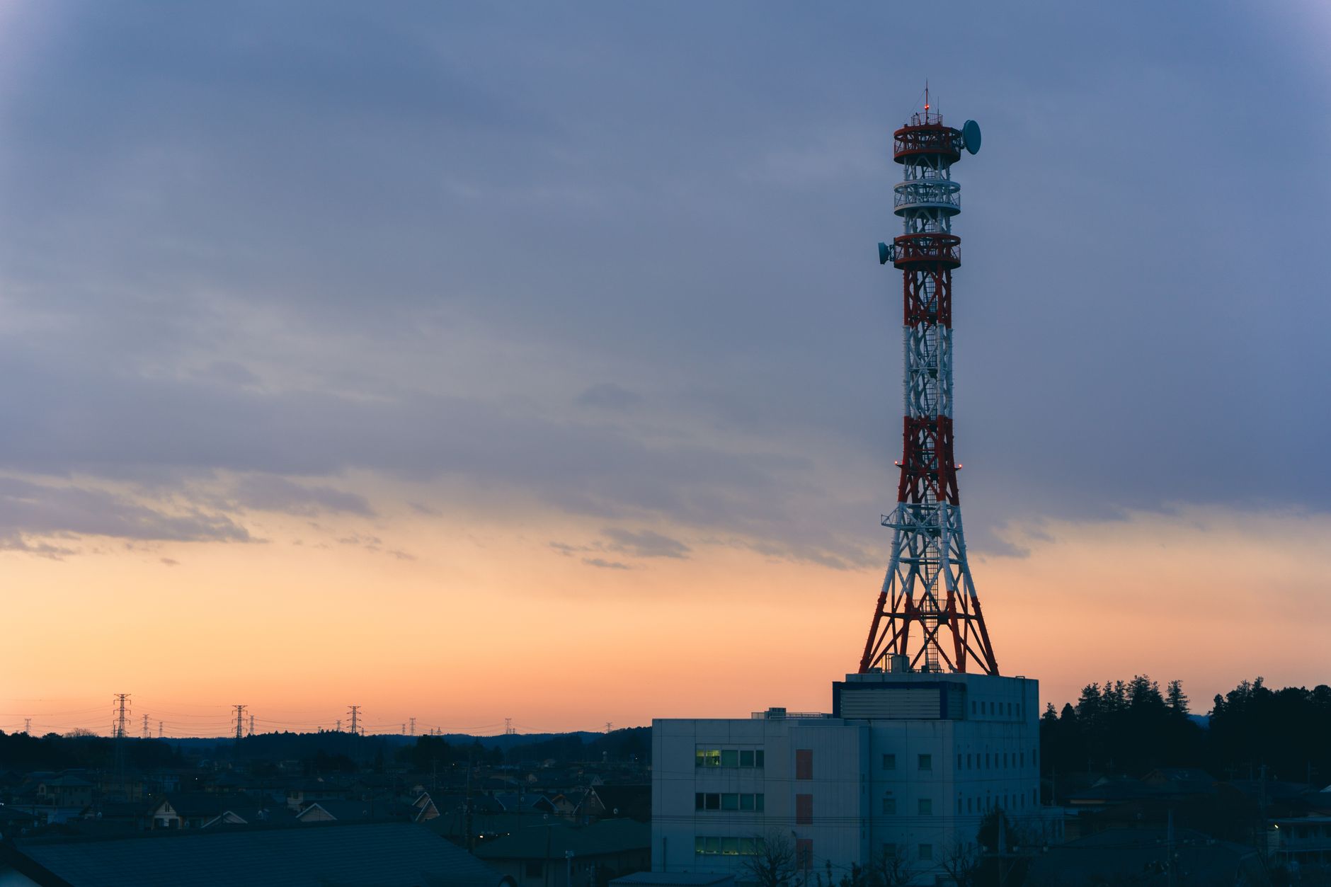 a rooftop RF antenna array pointed at an urban skyline at dusk, with multiple directional sensors mounted on a steel mast above a city monitoring facility