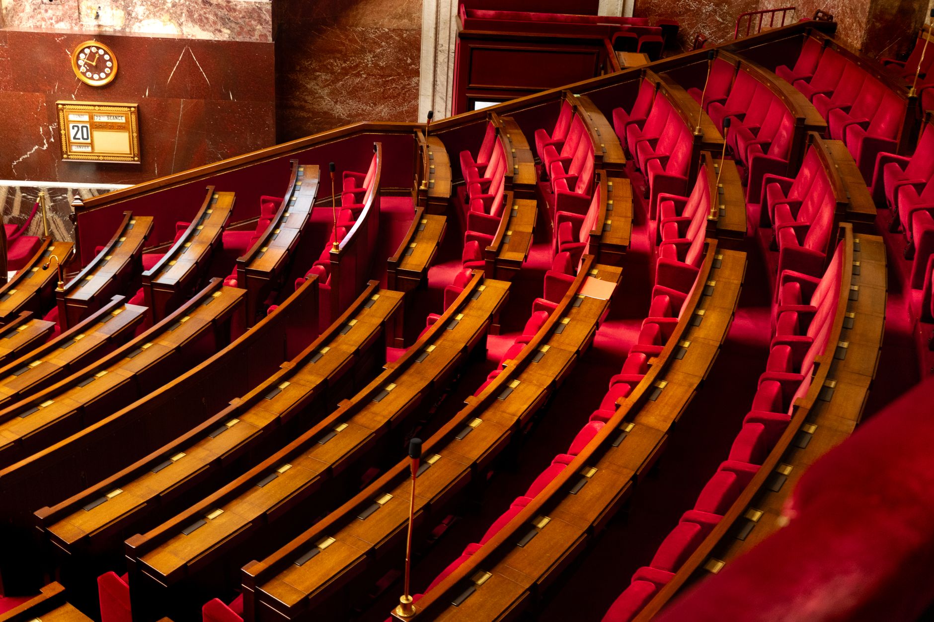 empty Senate chamber hearing room with rows of wooden desks and microphones, viewed from the gallery above