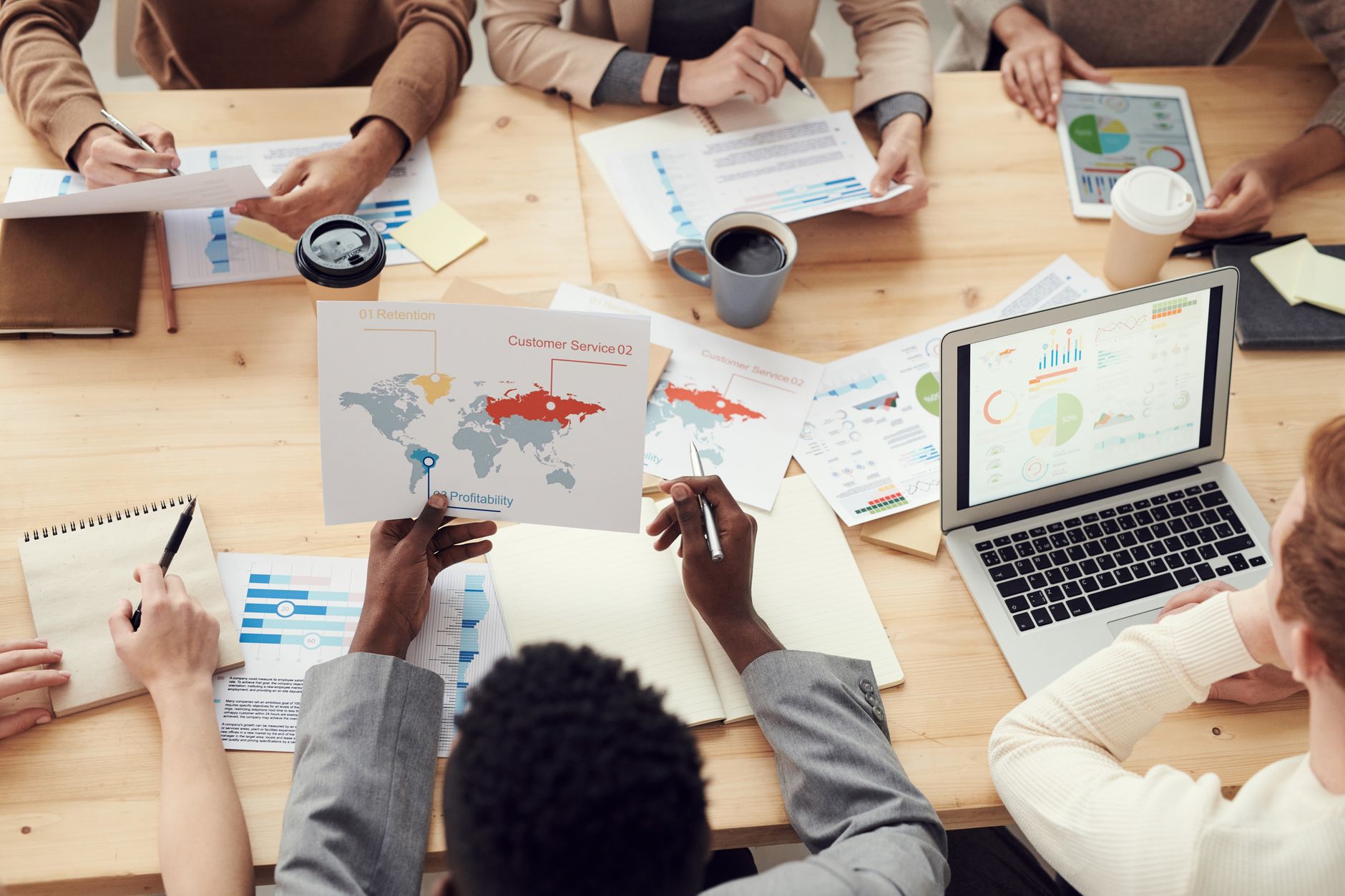 a close-up of an open laptop screen showing a startup pitch deck slide with charts and product screenshots, resting on a wooden conference table with a coffee cup nearby