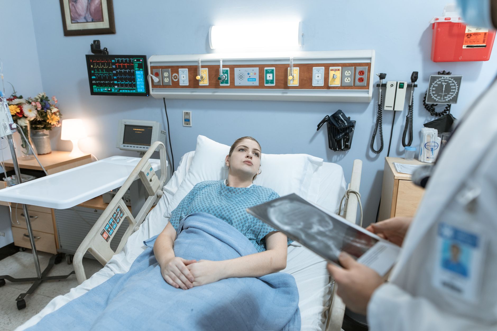 rows of hospital-grade IoT monitoring terminals mounted above patient beds in a modern ICU ward, screens displaying real-time vital sign dashboards