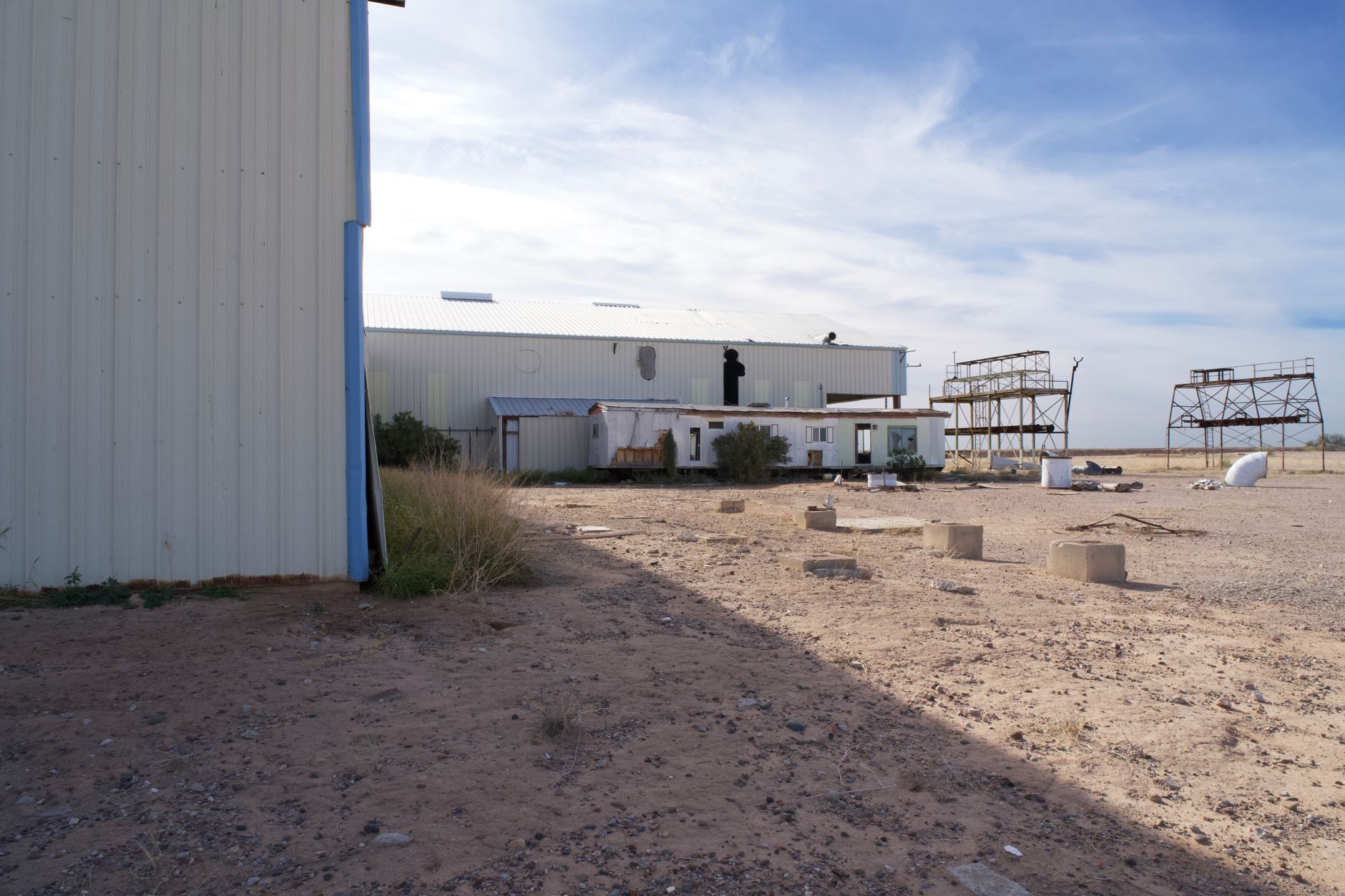 wide shot of a remote coastal industrial launch pad structure at dusk, surrounded by flat wetland terrain with no surrounding development visible