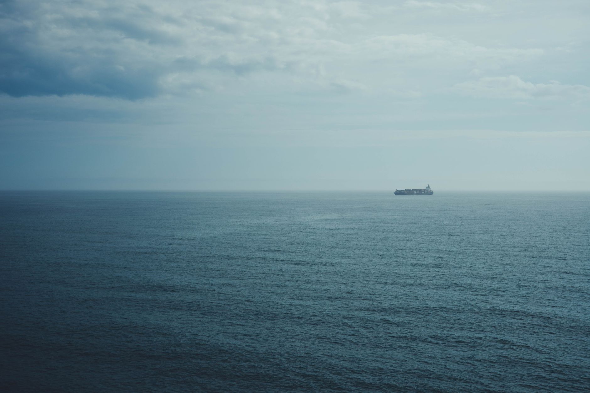a large white rocket stage being towed across open ocean by a heavy salvage vessel under clear skies, seen from a distance with calm blue water surrounding it