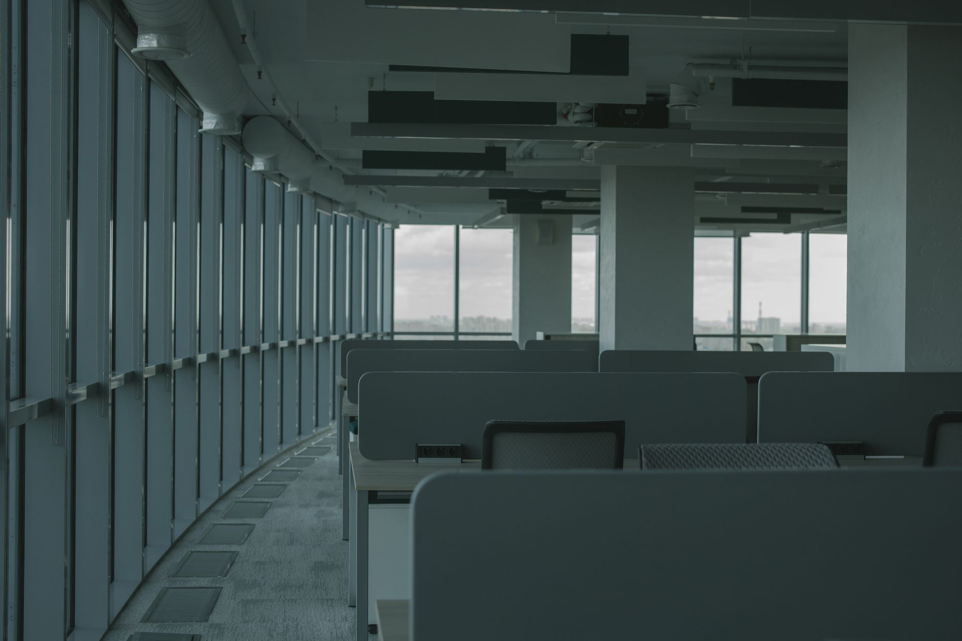 a sleek modern office interior with rows of workstations and tall windows overlooking a city skyline at dusk, workstations unoccupied