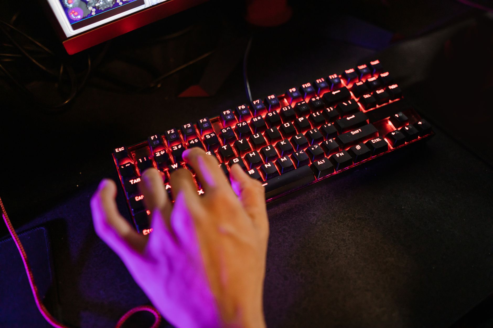 close-up of a mechanical gaming keyboard with per-key RGB lighting on a dark desk mat, keys slightly illuminated in a dark room
