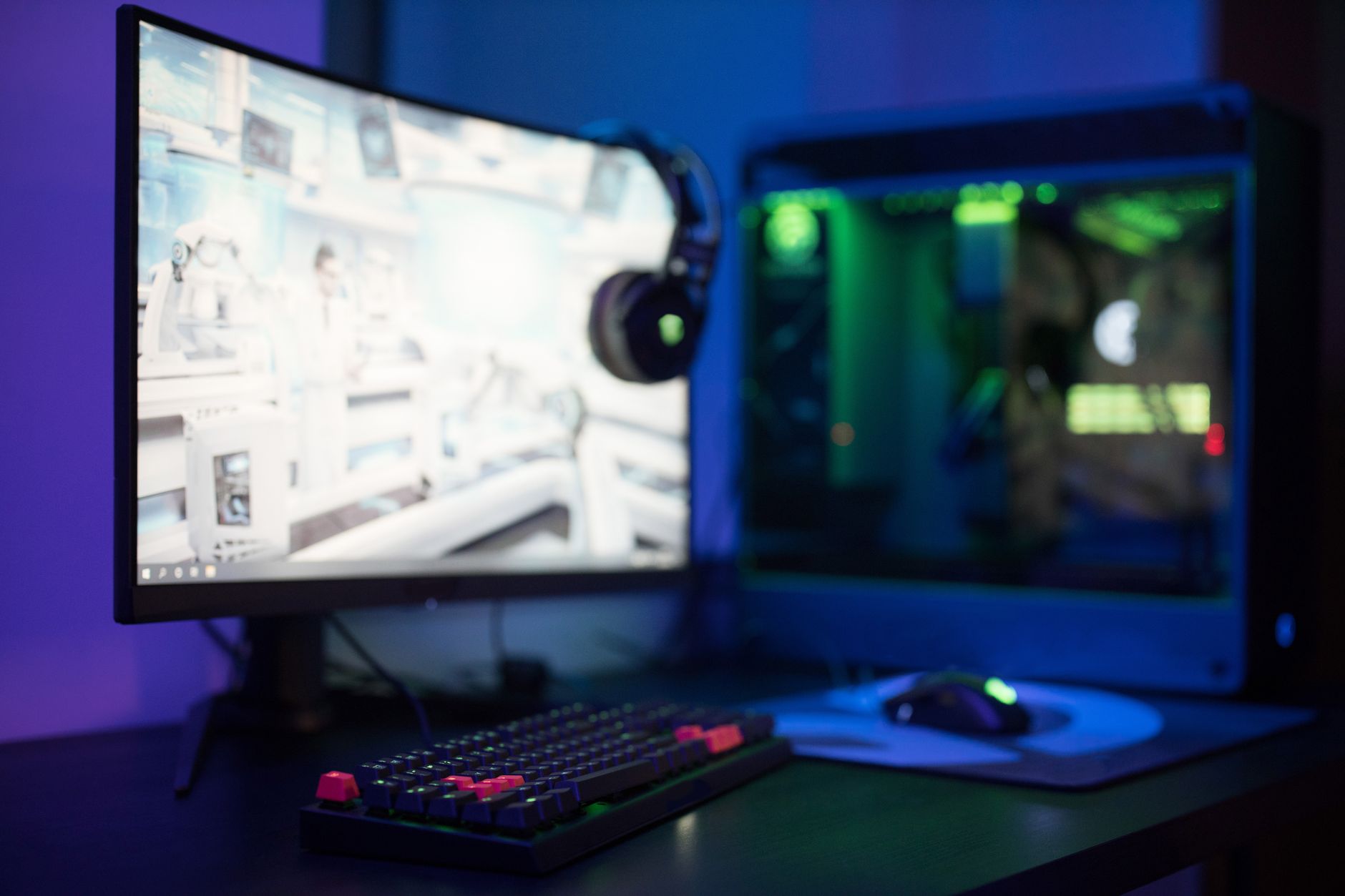 a wireless gaming headset resting on a stand beside a desktop monitor displaying a dark game environment