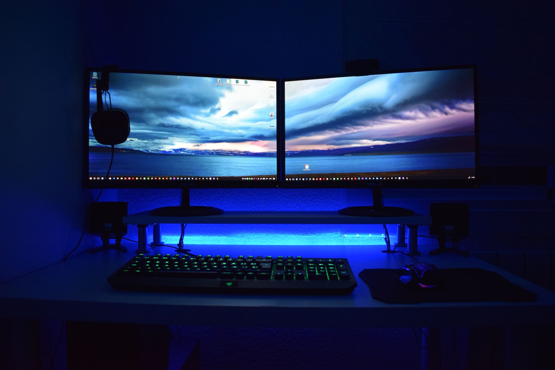 a cluttered gaming setup with multiple monitors displaying disconnected or error screens, ethernet cables visible on a wooden desk in a dimly lit room