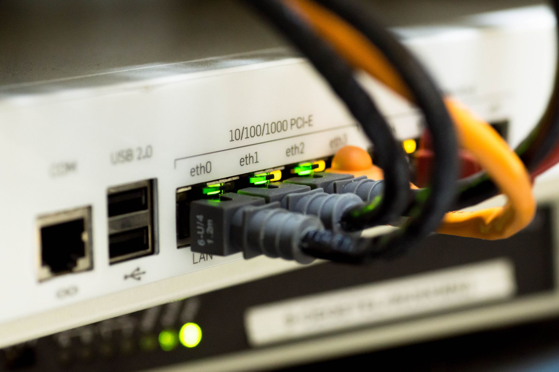 A small Android TV streaming stick plugged into the HDMI port on the back of a large flat-screen television, with a cluttered home network router visible on a shelf nearby