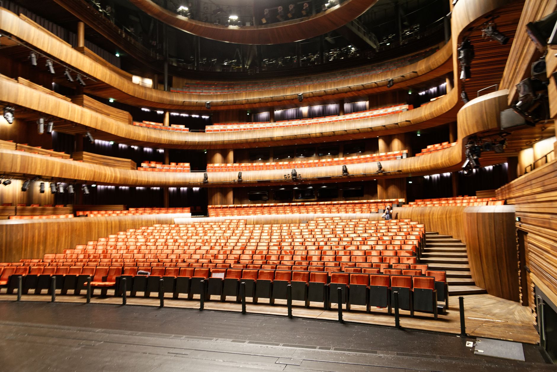 wide-angle view of a sleek Manhattan event venue interior with rows of chairs facing a lit stage, floor-to-ceiling windows overlooking the city skyline at dusk