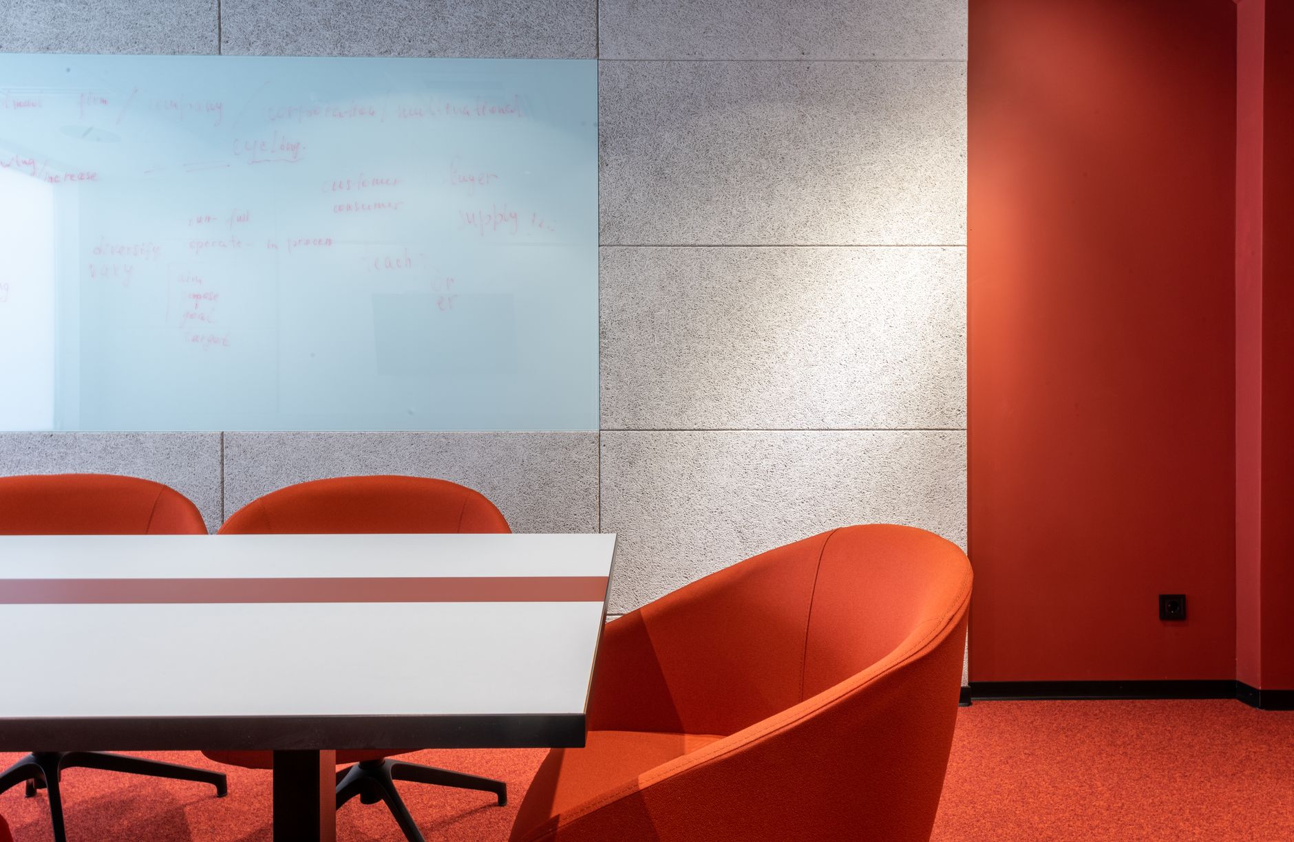 a glass-walled conference room interior with a large wall-mounted display showing a project roadmap and timeline, notebooks and laptops on the table, no faces visible