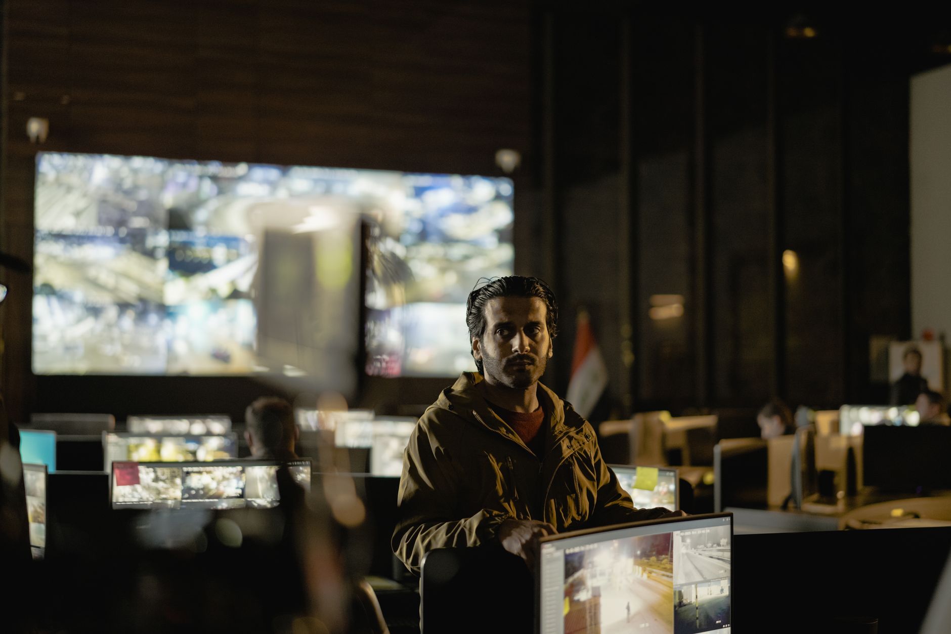 a curved array of security operations center monitors displaying network topology maps and live threat alert dashboards in a darkened room