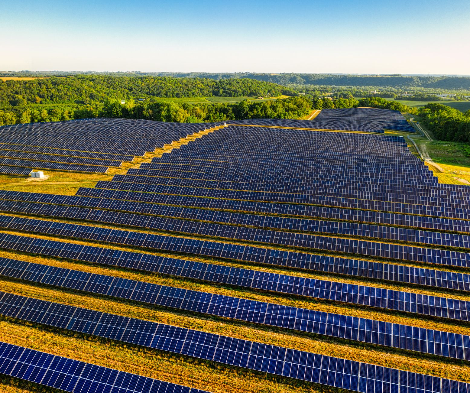 aerial view of a sprawling utility-scale solar farm with rows of photovoltaic panels stretching to the horizon under a clear blue sky, no people visible