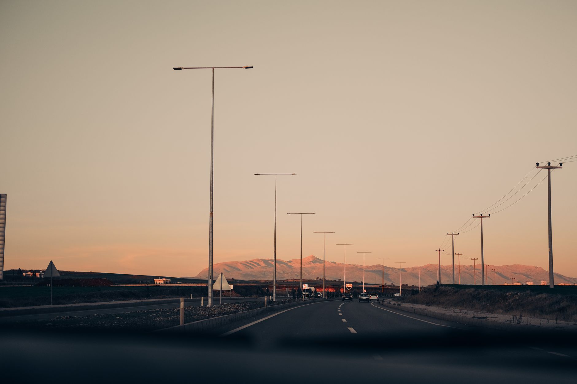 a highway intersection at dusk with overhead roadside communication towers mounted on signal poles, no vehicles visible, wide environmental shot showing infrastructure against a darkening sky
