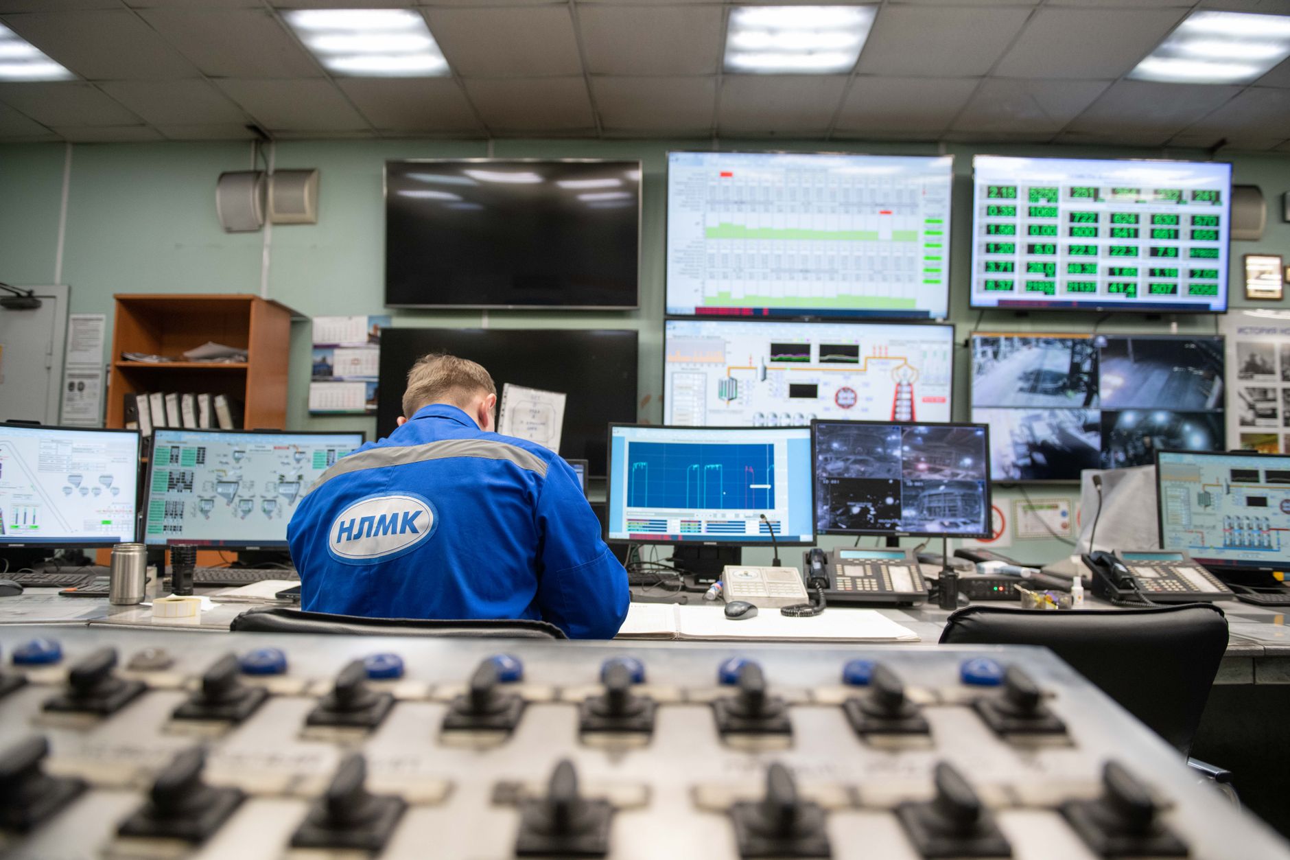 a broadcast television control room with multiple monitor screens showing live news feeds and production dashboards, empty operator chairs visible