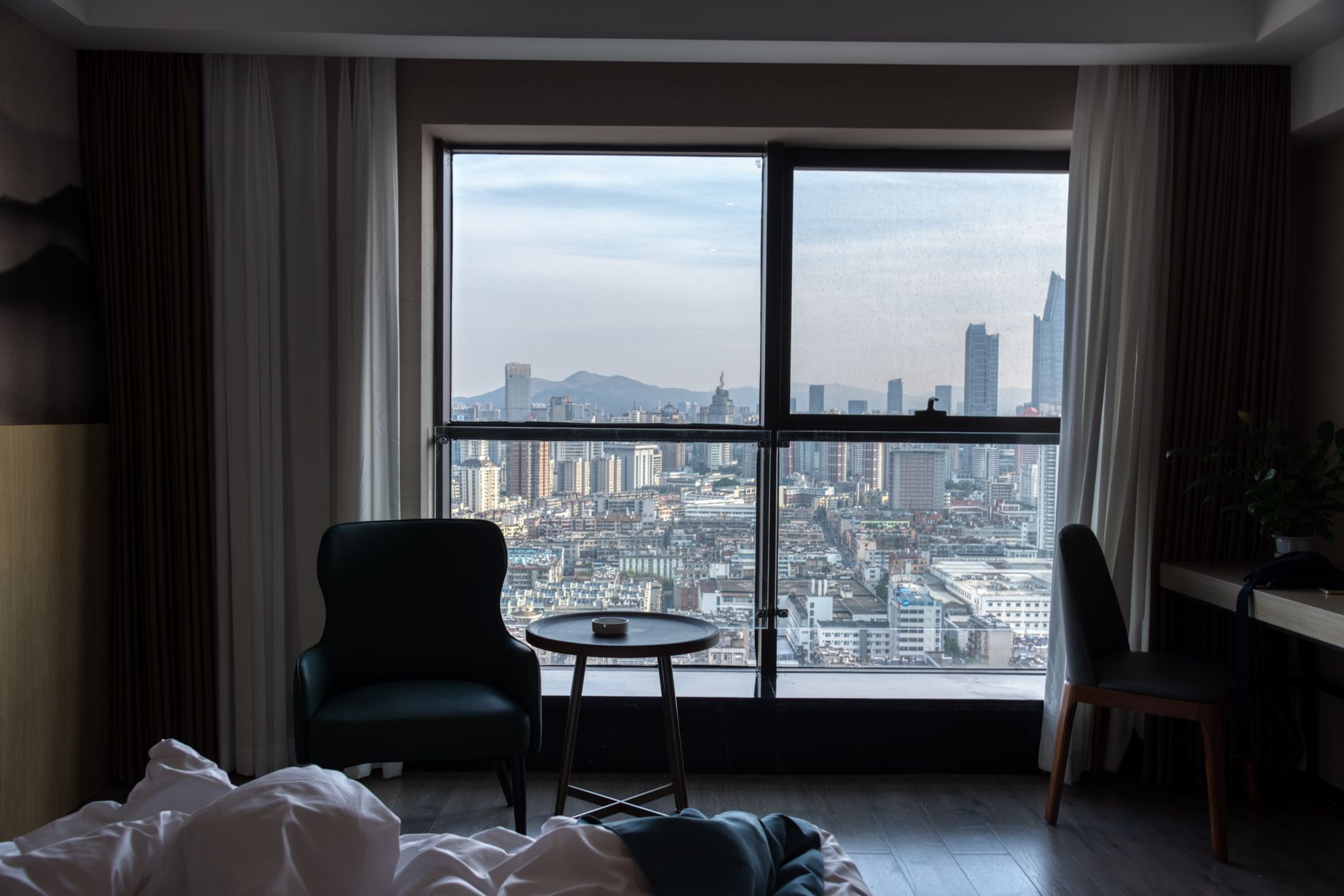 a modern air purifier unit on a wooden surface in a sunlit urban apartment with hazy city skyline visible through the window behind it