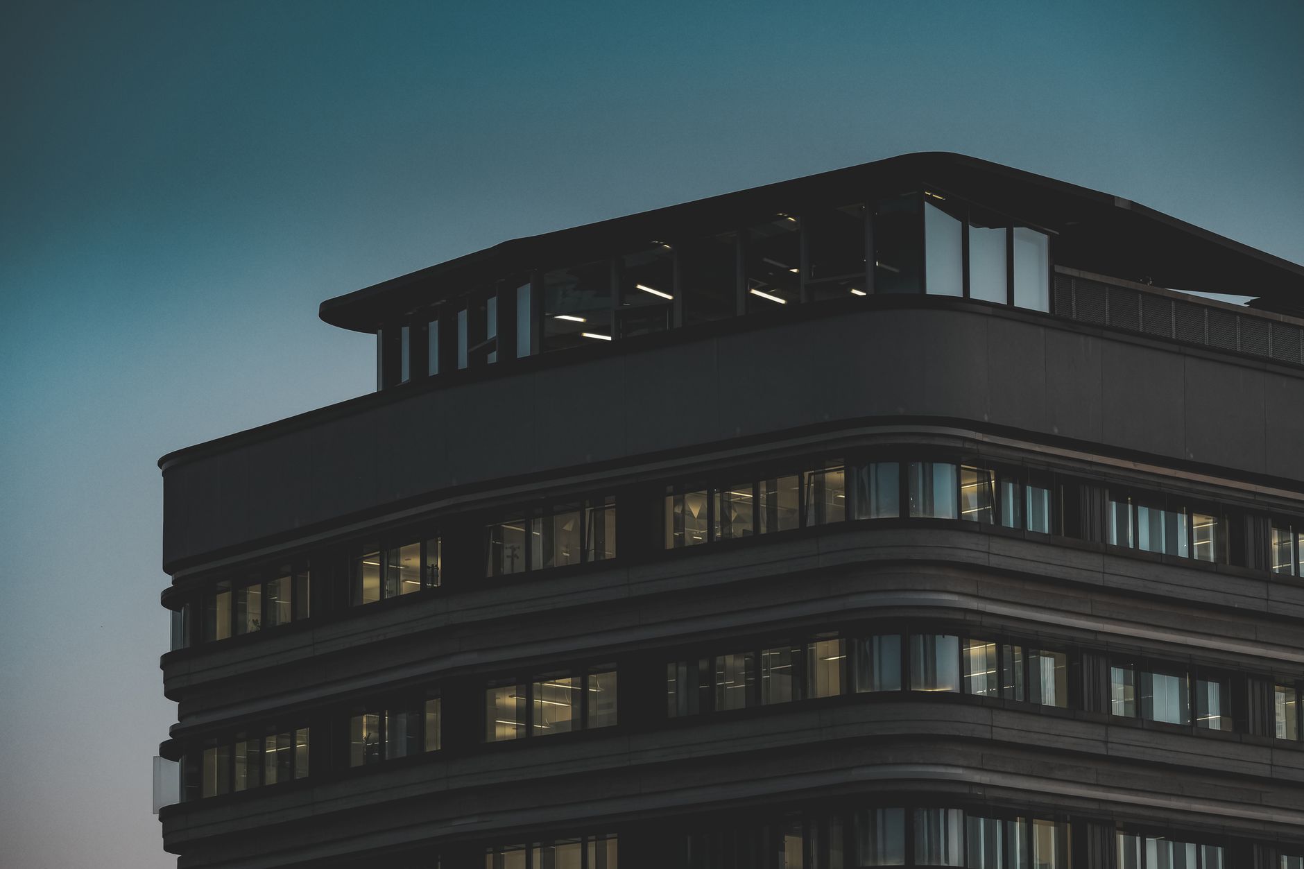 exterior of a modern glass-and-steel investment firm headquarters at dusk, with city lights reflected in the facade