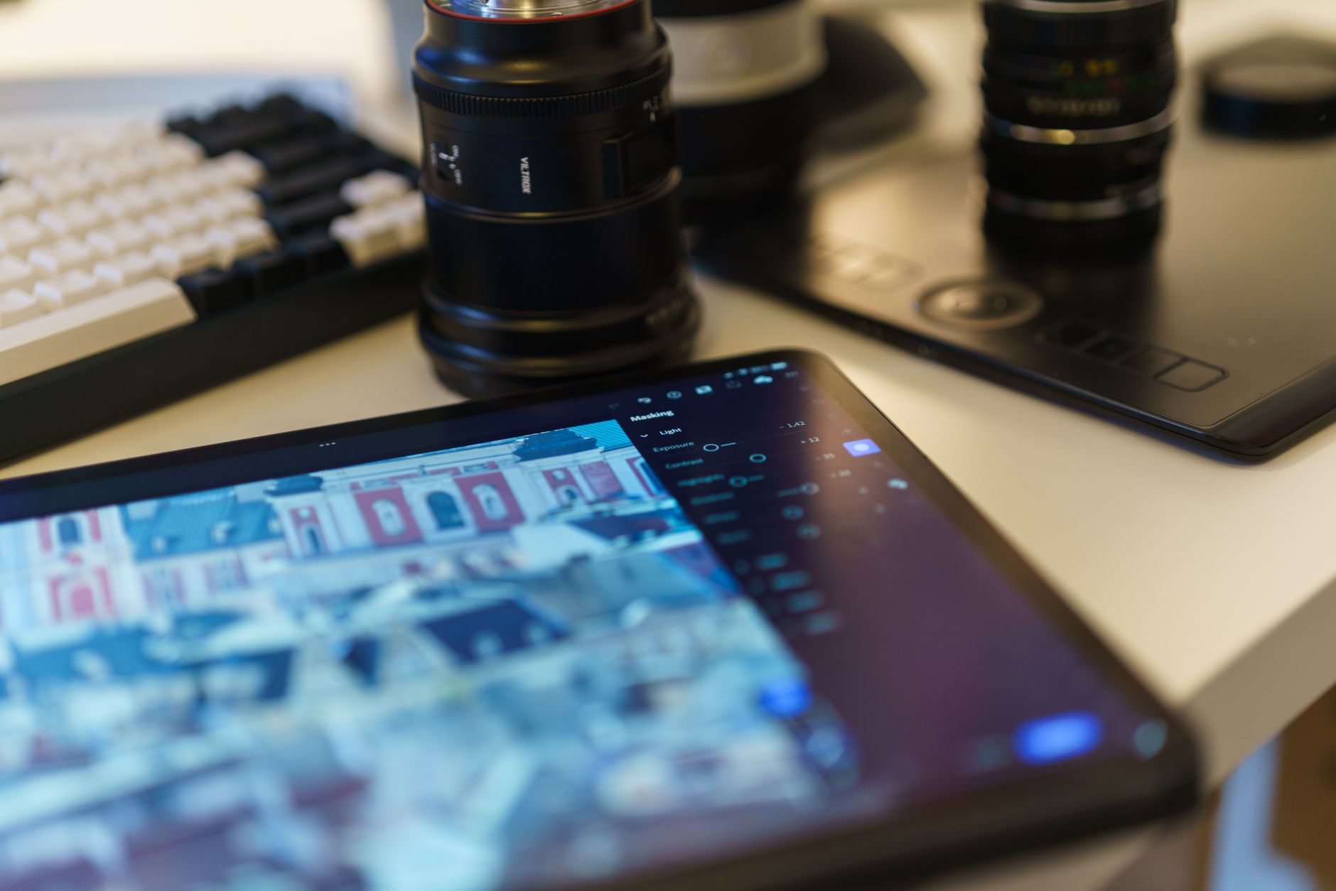 an Android tablet resting on a desk beside a small camera and a pair of wireless earbuds, with a video editing timeline visible on the tablet screen