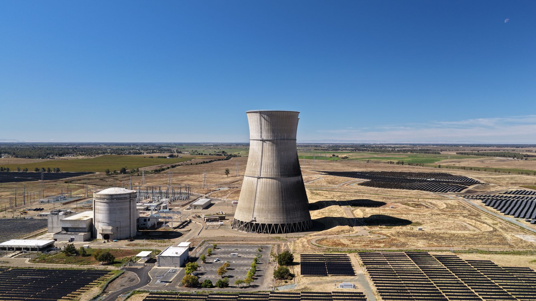 an aerial view of a large data center campus under construction in an arid landscape, surrounded by solar panels and utility infrastructure