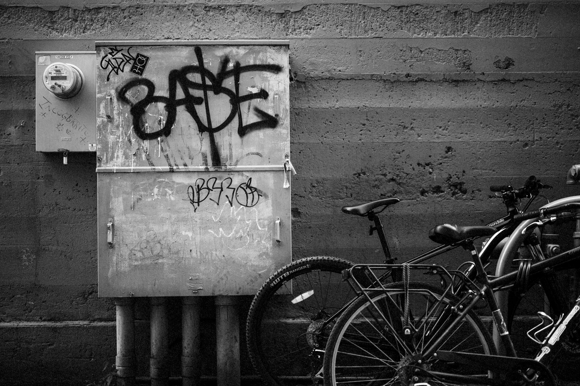 A sleek, matte-finish electric bicycle leaning against a concrete wall in an urban garage, with no rider present, overhead industrial lighting casting sharp shadows across the frame geometry