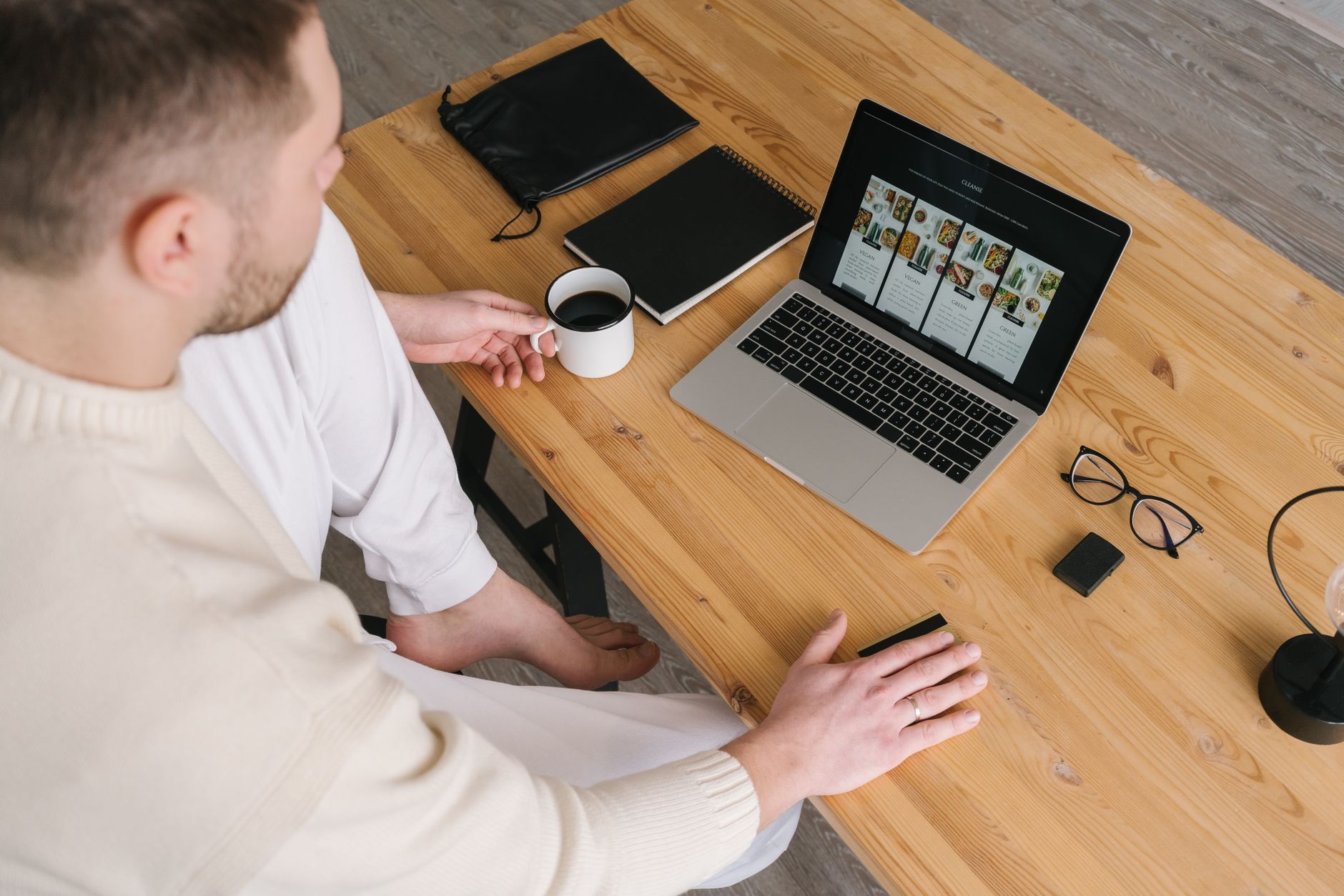 a laptop screen showing an e-commerce product grid with a browser address bar, sitting on a wooden desk beside a coffee cup