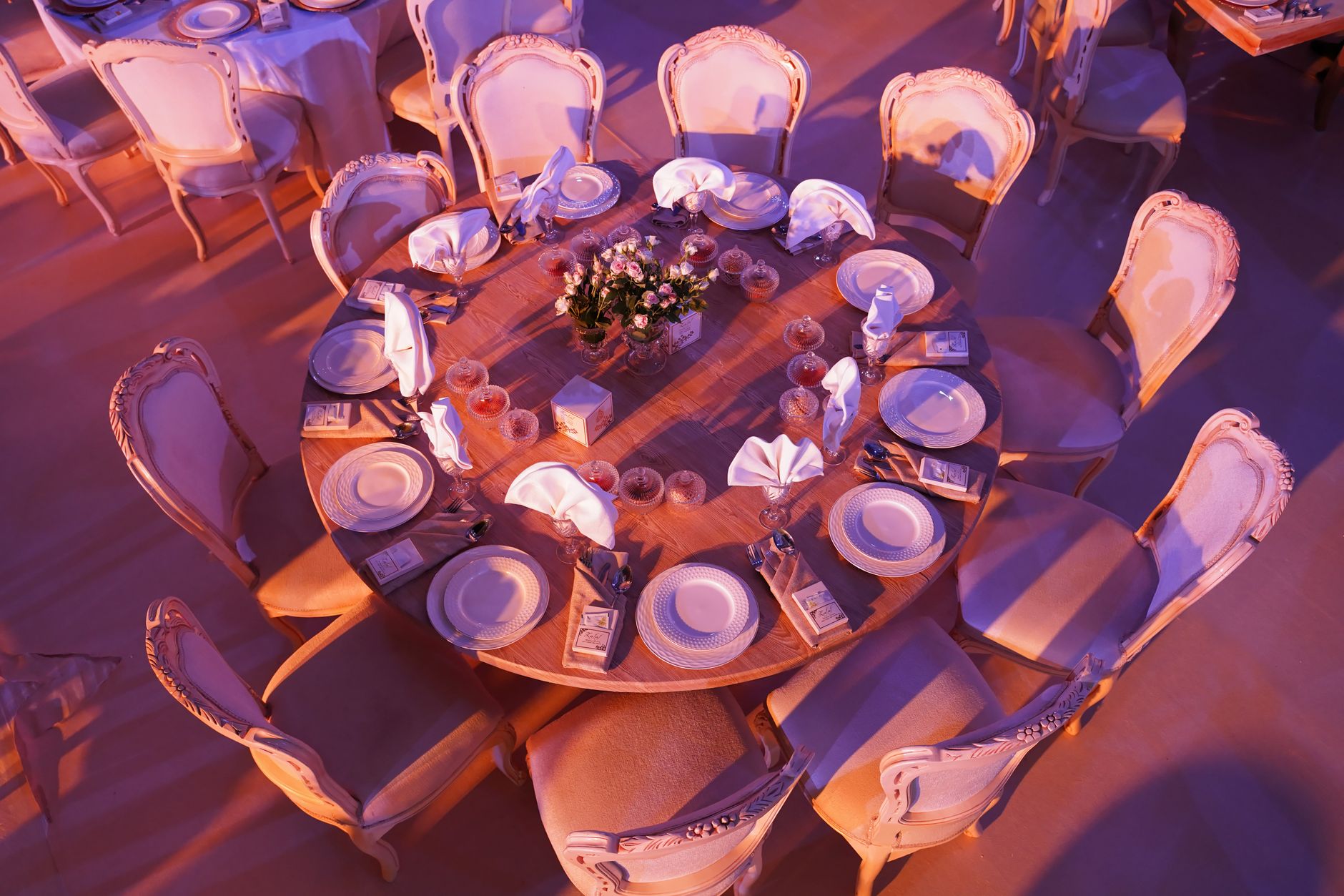 an empty formal dining room inside a historic government building, long mahogany table set with glassware and folded napkins, chandelier overhead, tall windows with evening light