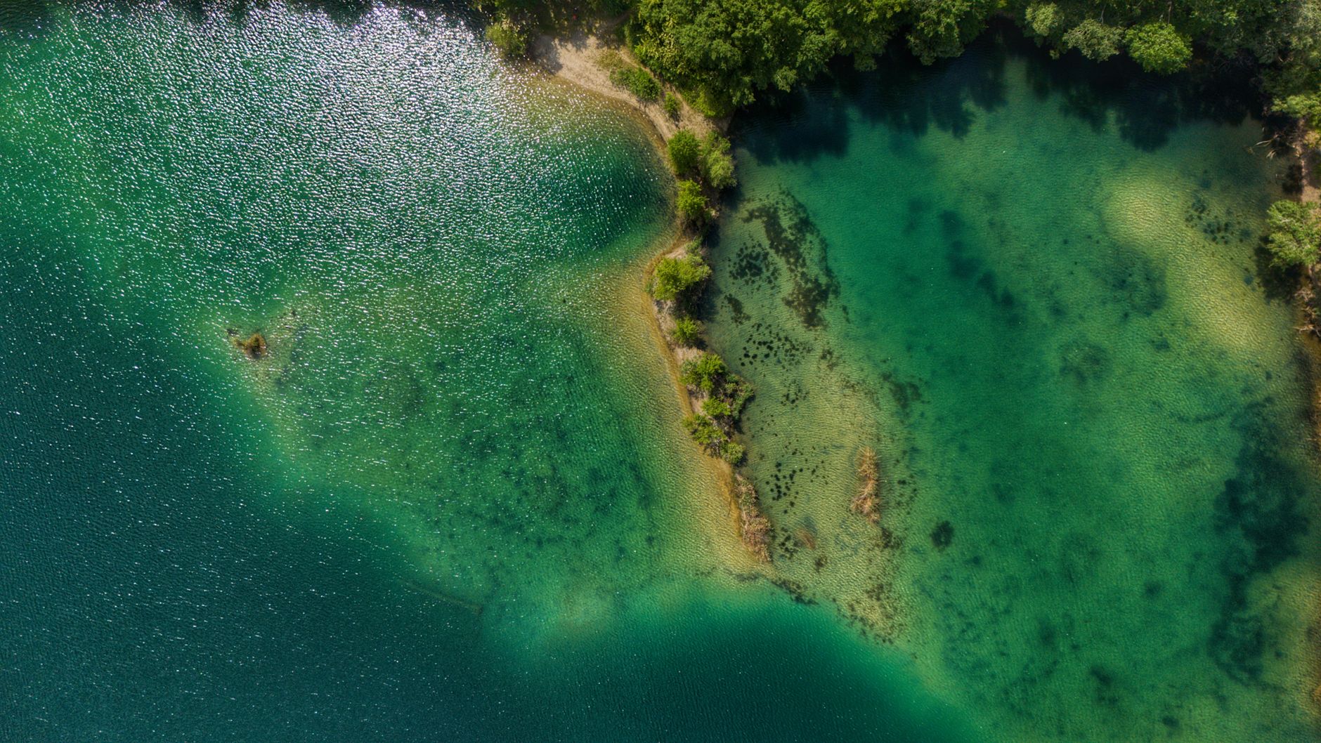 a wide aerial view of a large lake shoreline where a border region meets open water, under overcast skies with no visible landmarks or signage