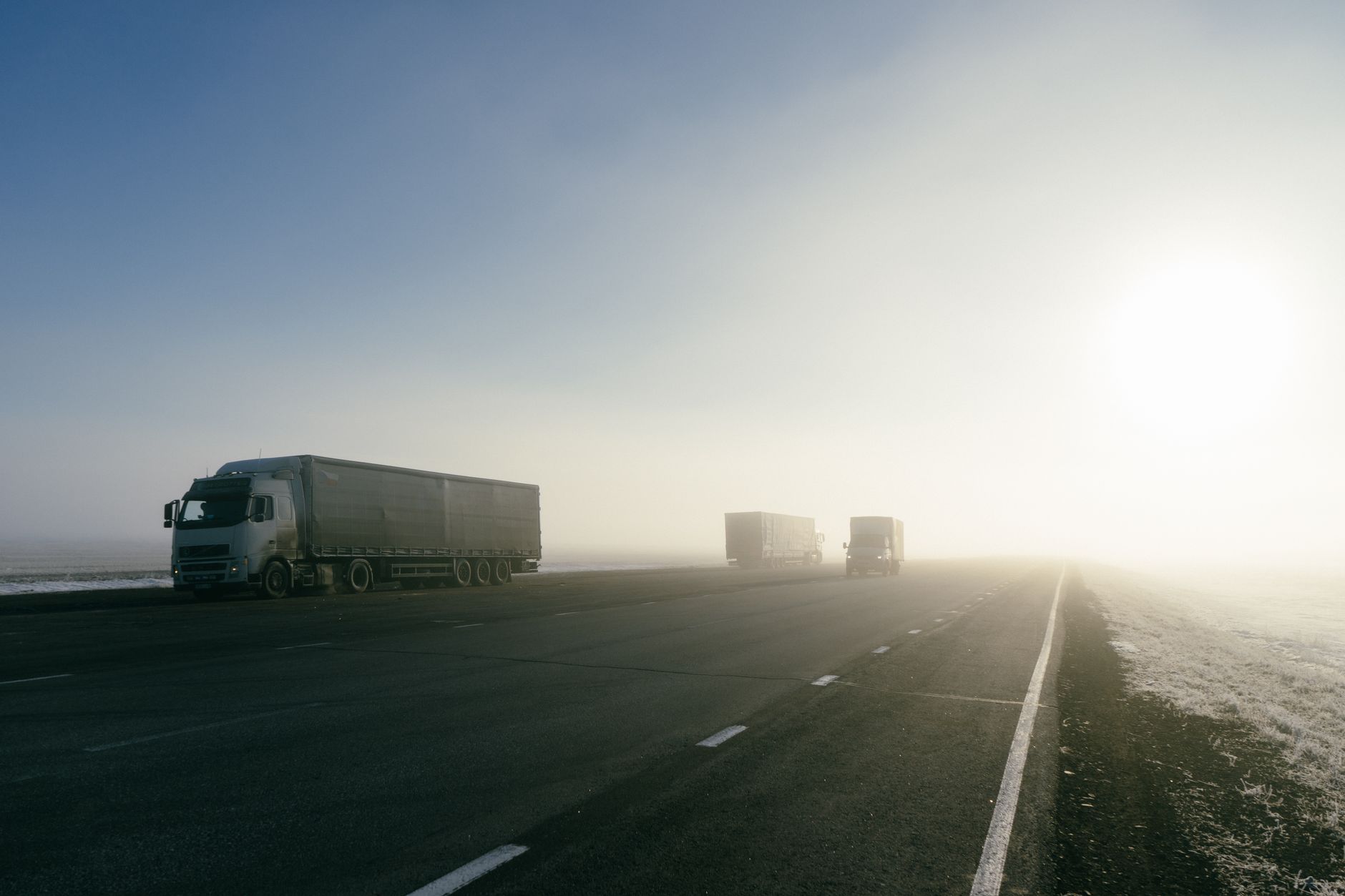 rows of parked Class 8 freight trucks in a large logistics yard at dusk, dock doors visible in the background, no people in the foreground