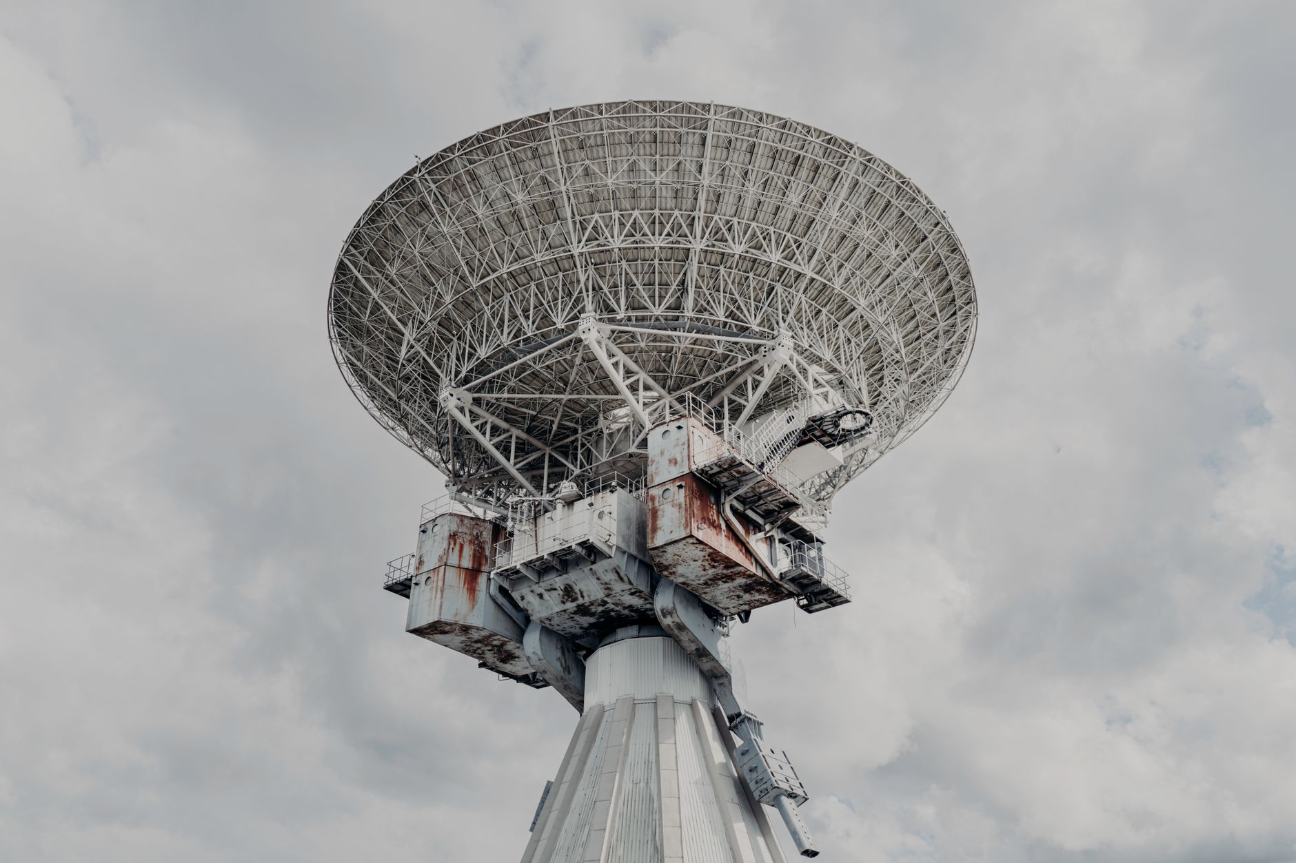 a close-up of a deep-space antenna dish pointed toward the sky on a sun-baked desert landscape, with mission control equipment visible in a low structure behind it