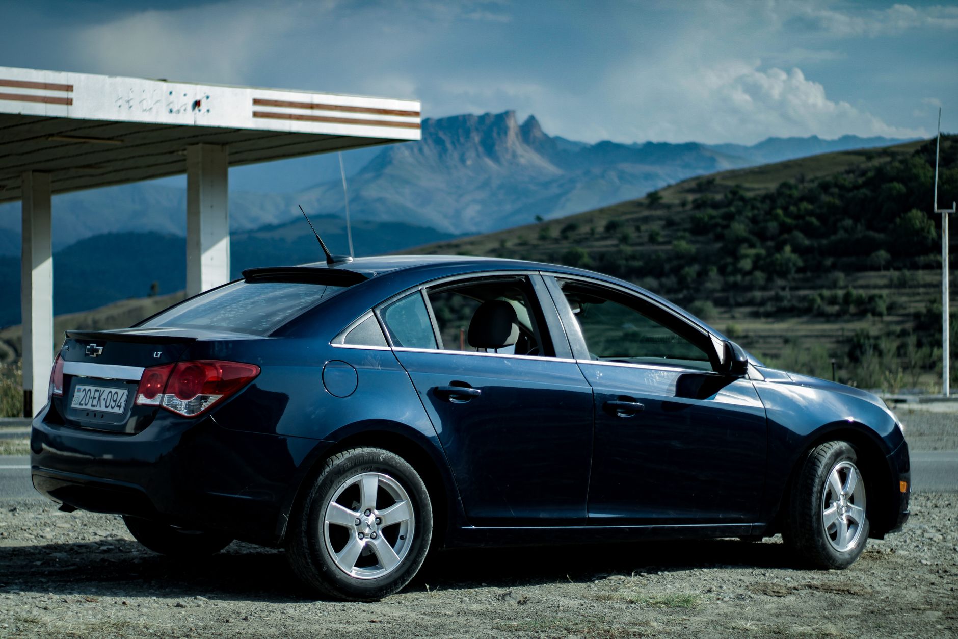 A sleek silver electric sedan parked on a wide open highway at dusk, mountains visible in the background, no people visible
