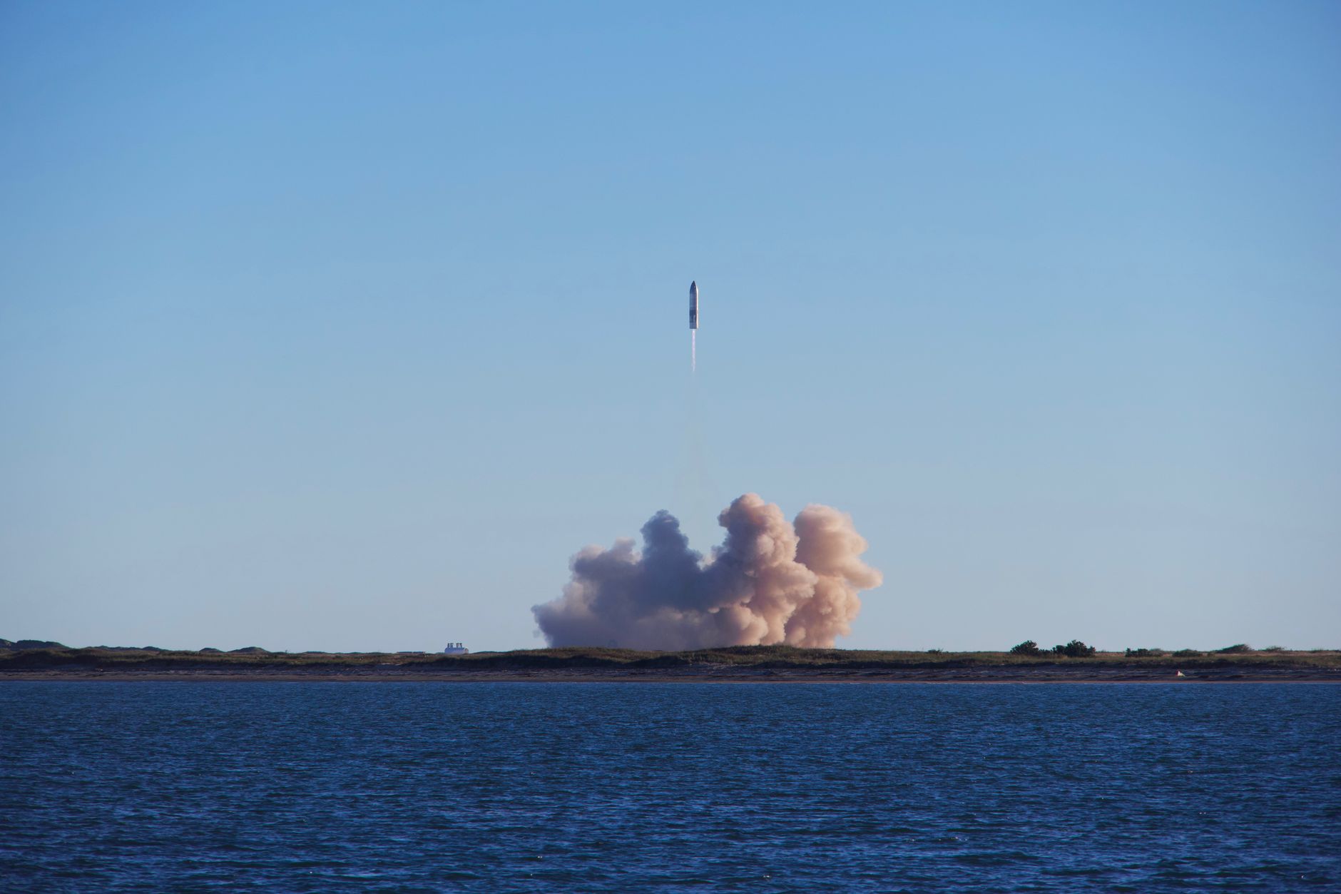 a small orbital rocket standing on a compact coastal launch pad at dawn, ocean visible in the background, surrounded by minimal ground support equipment