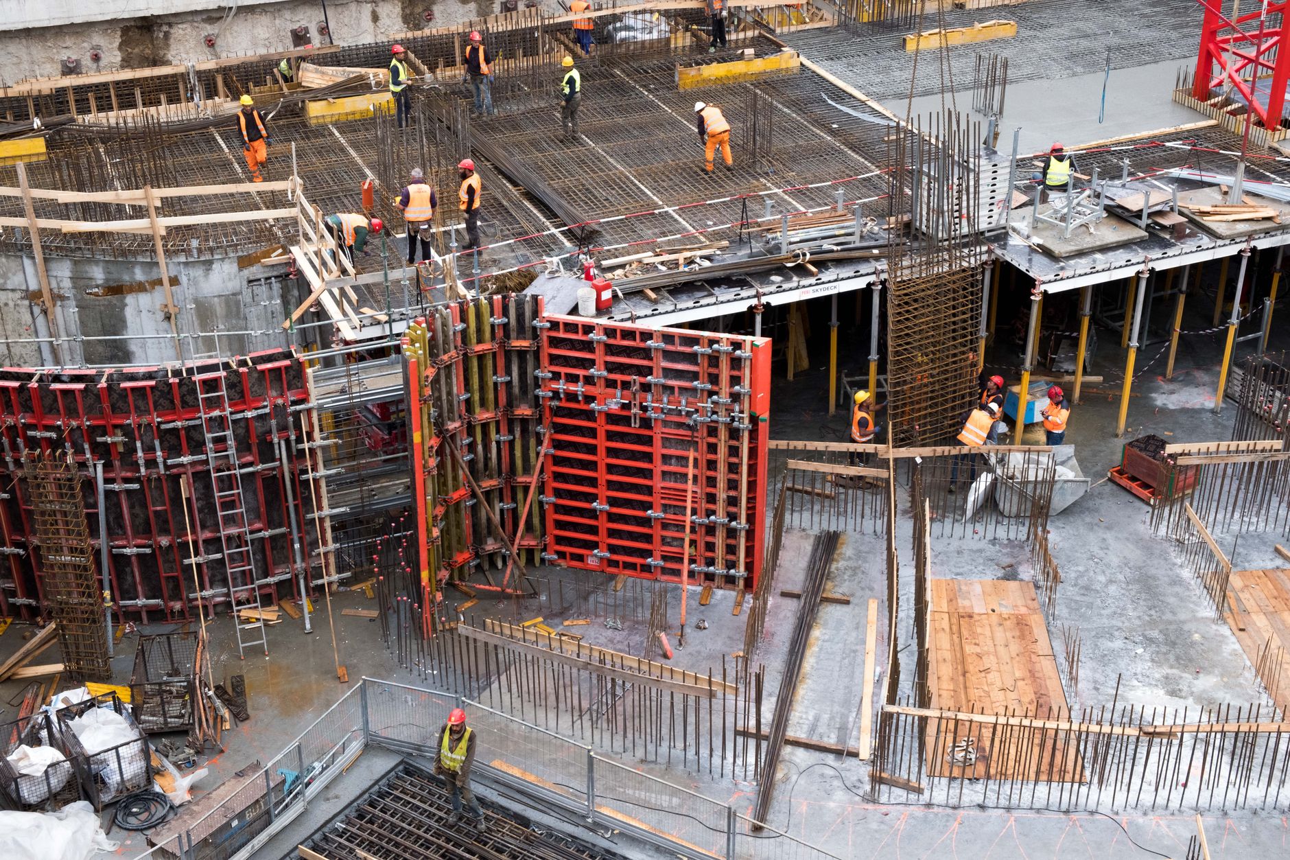 a construction worker in a hard hat walking through a partially built concrete floor of a high-rise building, with structural columns and open sky visible above
