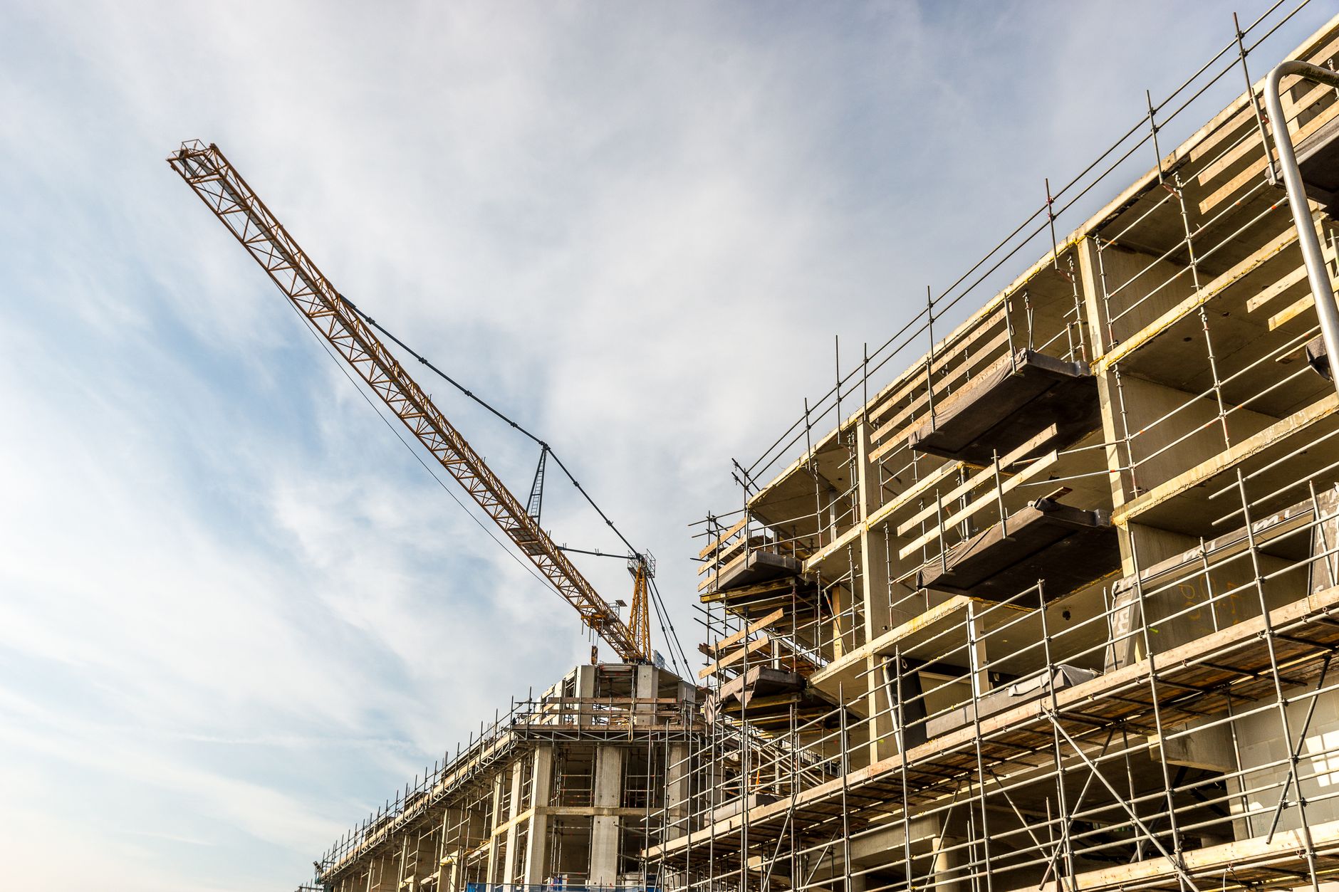 a wide-angle view of a large commercial construction site at ground level, with steel frameworks, cranes, and stacked building materials spread across the floor plate