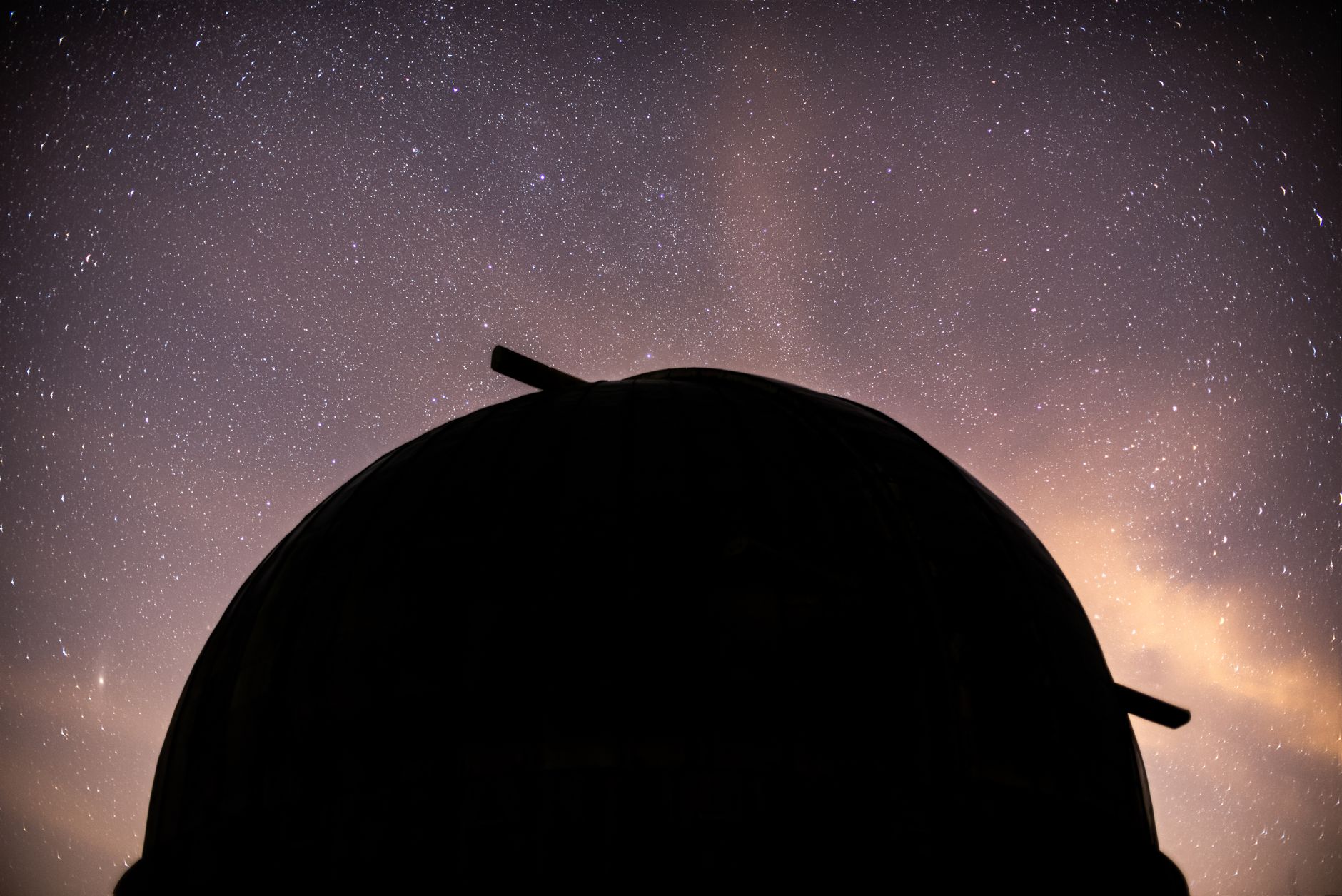 a ground-based telescope dome open at night under a clear sky with the Milky Way visible above a high-altitude observatory plateau