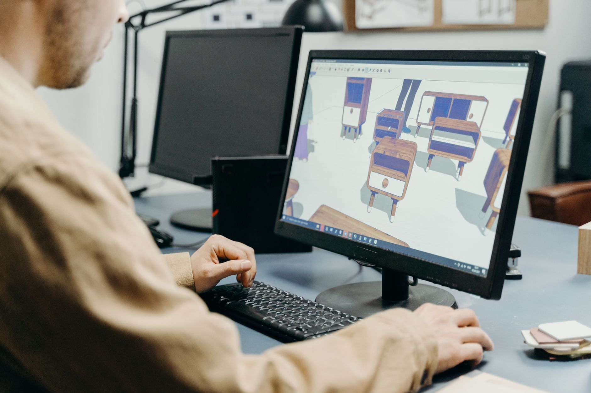a computer monitor displaying a 3D CAD model of a precision aerospace bracket with color-coded CNC toolpath lines overlaid on the geometry