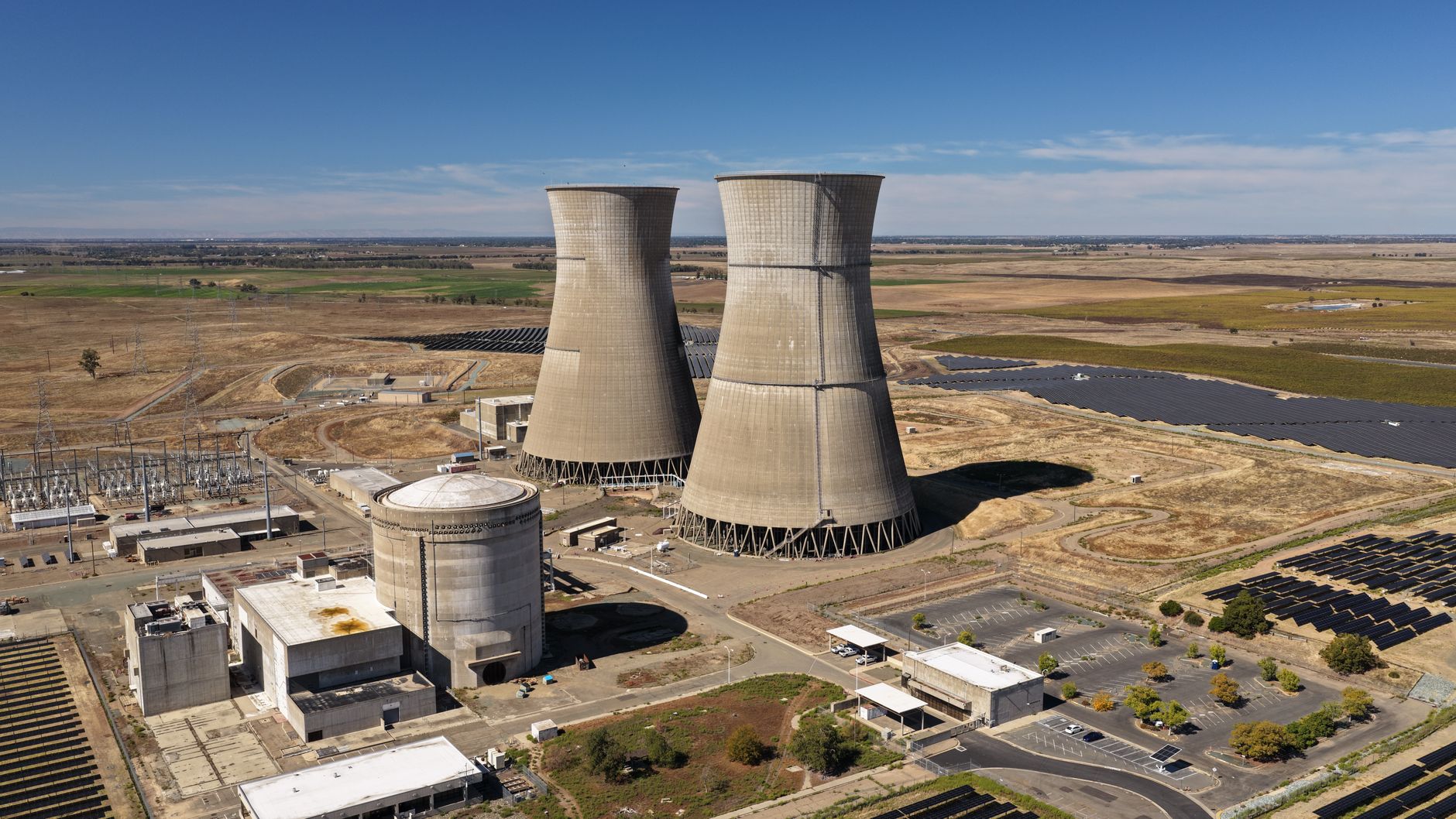 aerial view of a large-scale data center campus under construction in an arid landscape, with visible cooling infrastructure and power substations