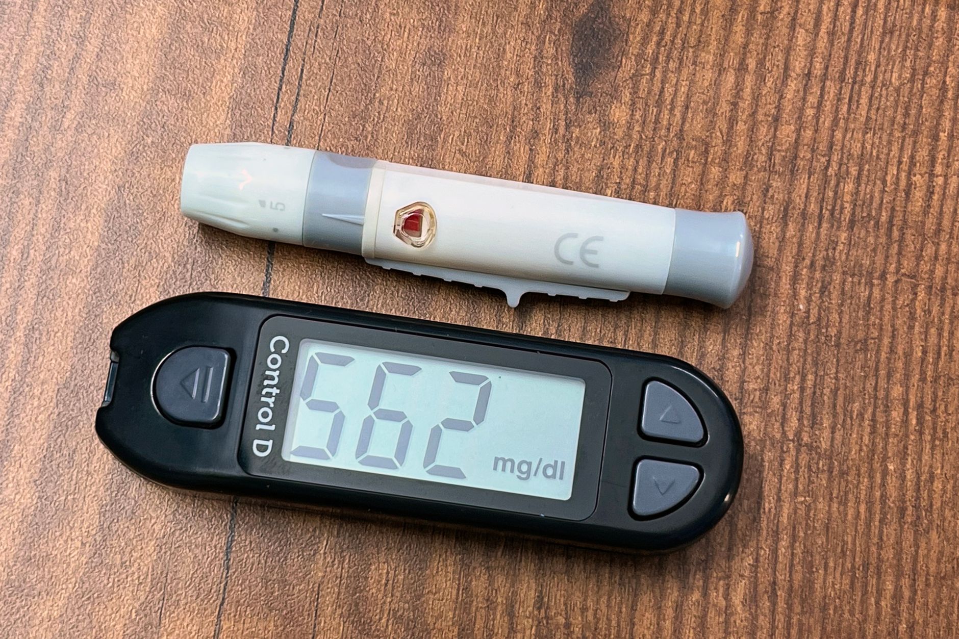 a continuous glucose monitor mounted on a forearm resting on a desk beside a smartphone displaying a glucose trend graph
